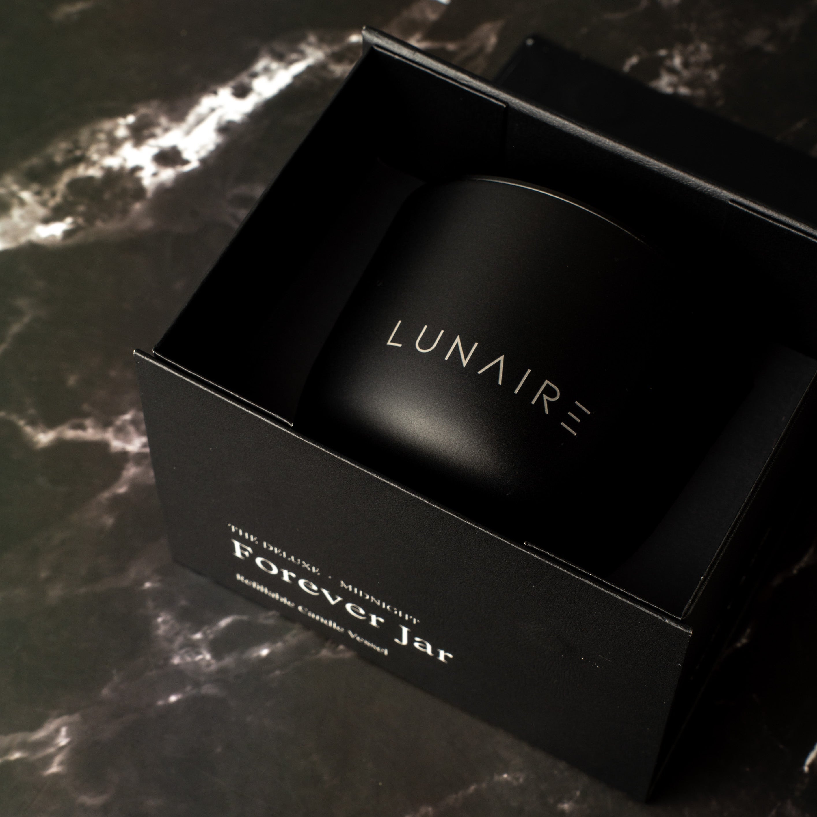 Black refillable candle jar with 'LUNAIRE' branding on a dark marble surface