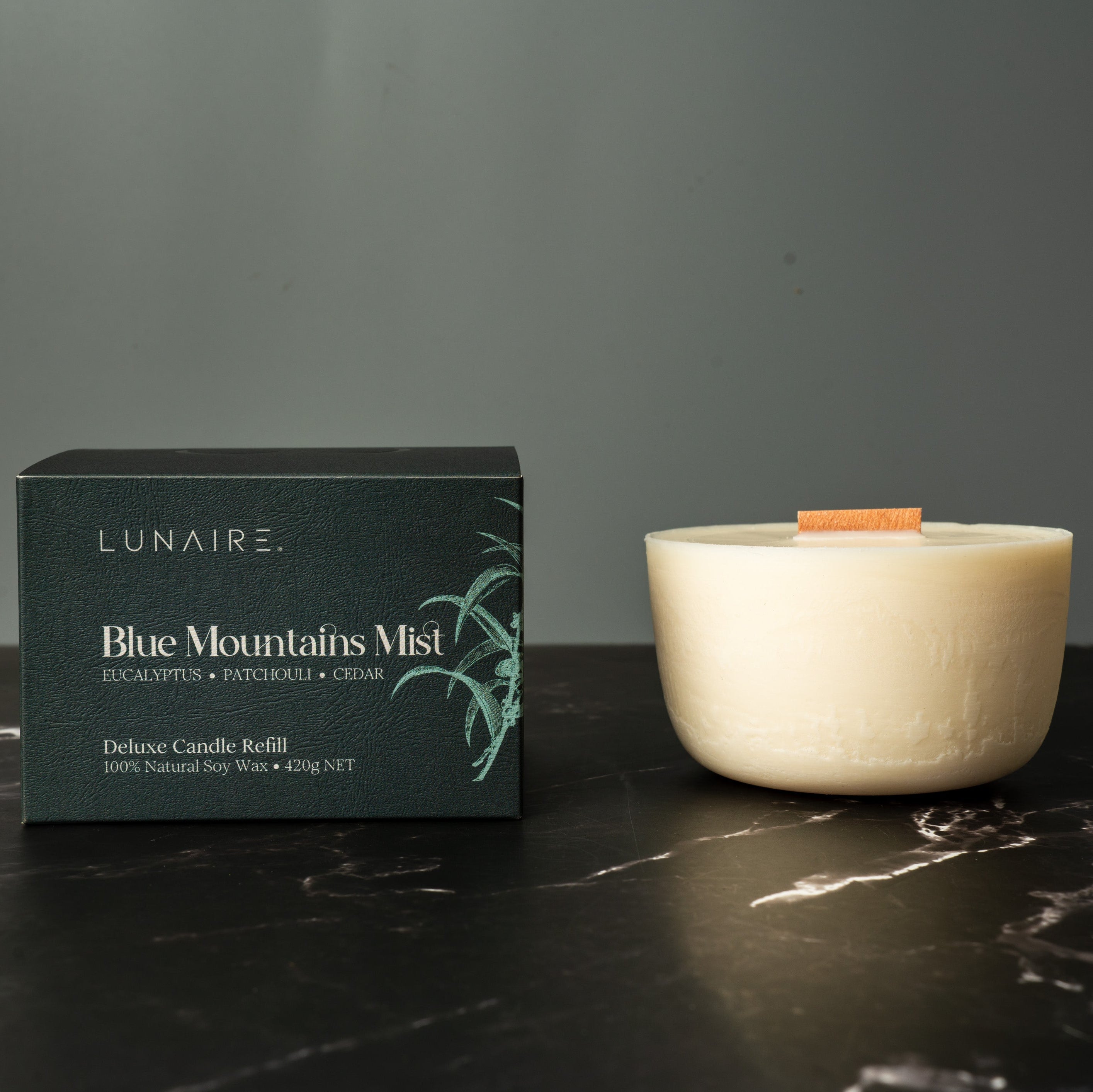 Lunaire Blue Mountains Mist candle and packaging on a dark surface with a gray background