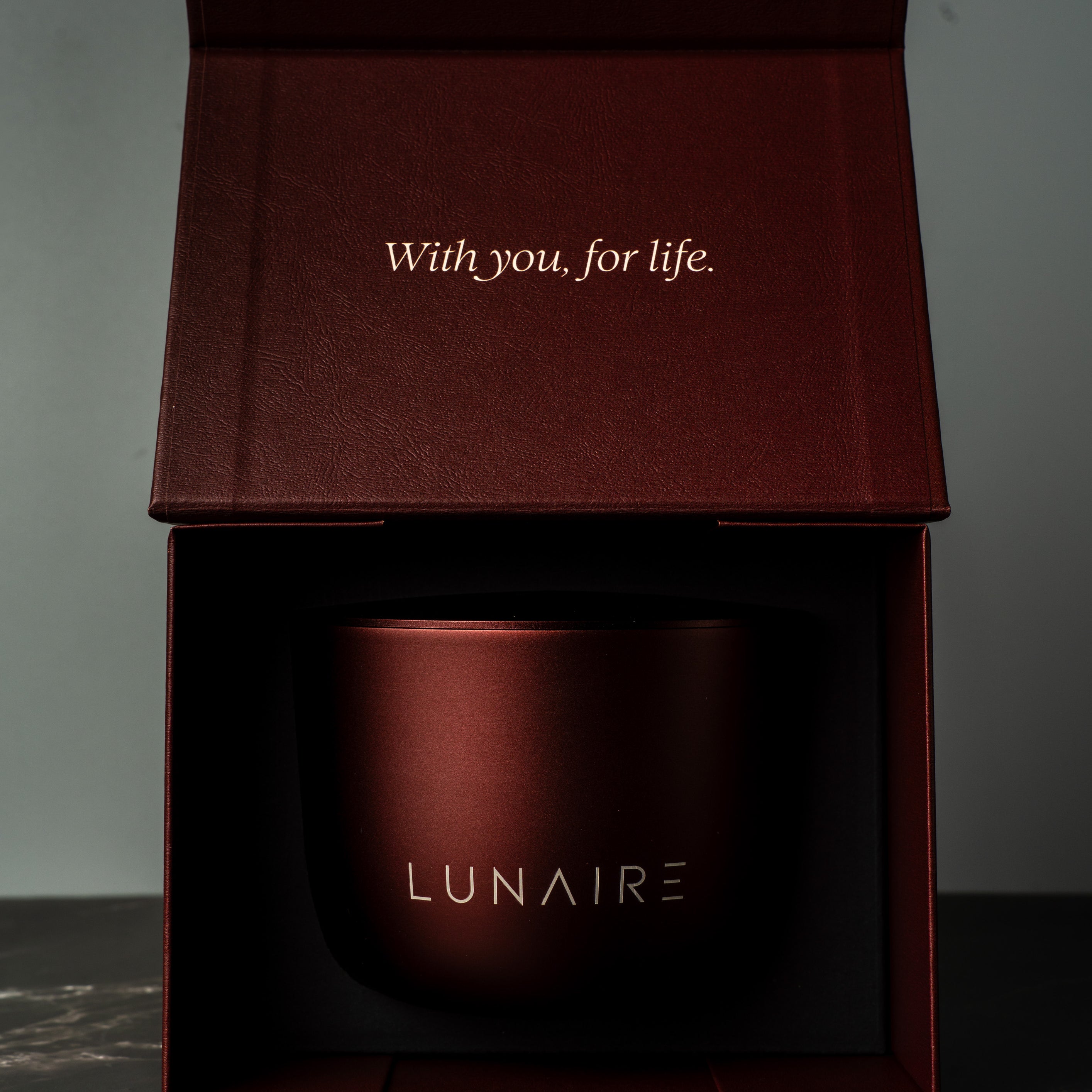 Red aluminium refillable candle jar with 'LUNAIRE' branding in an open box on a dark surface.