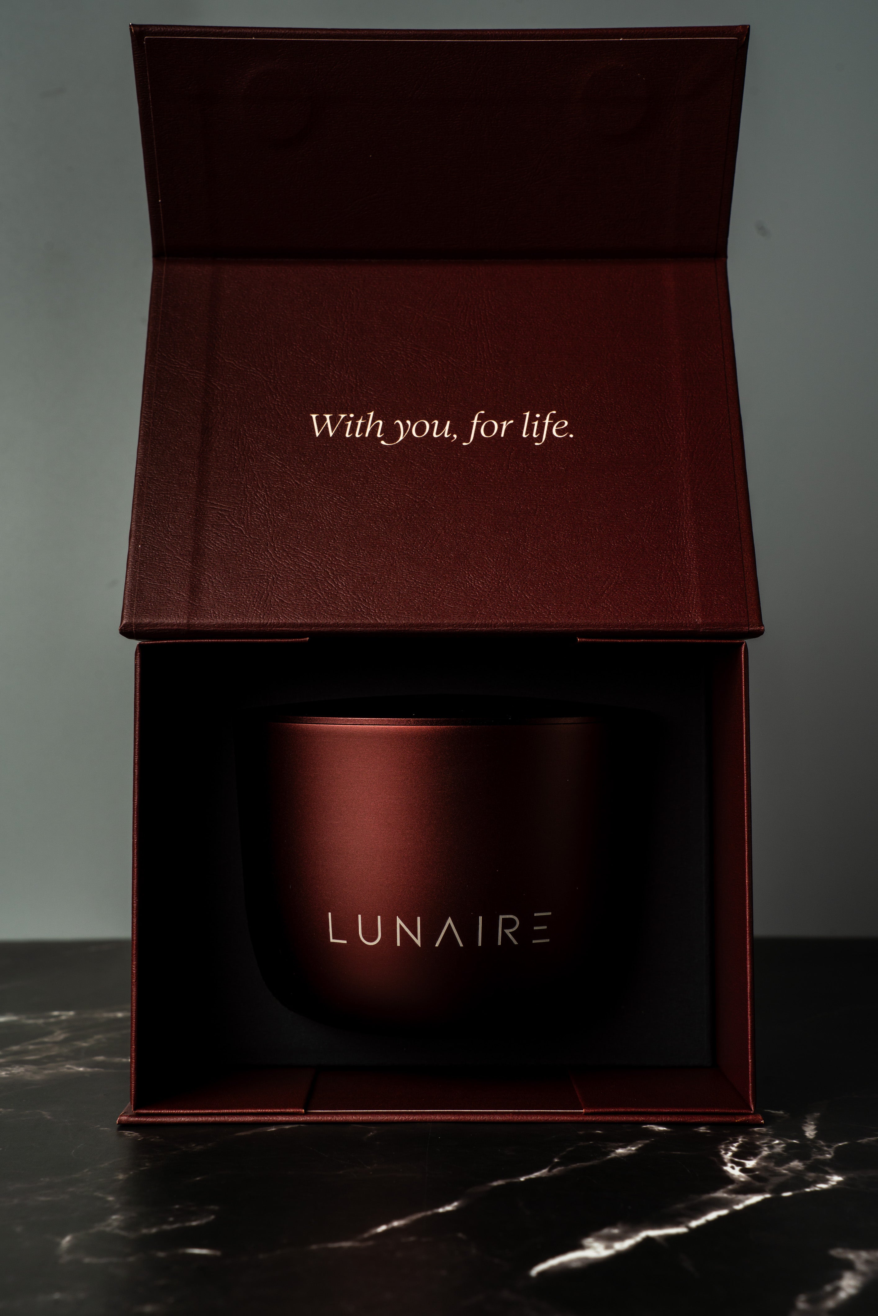 Red aluminium refillable candle jar with 'LUNAIRE' branding in an open box on a dark surface.
