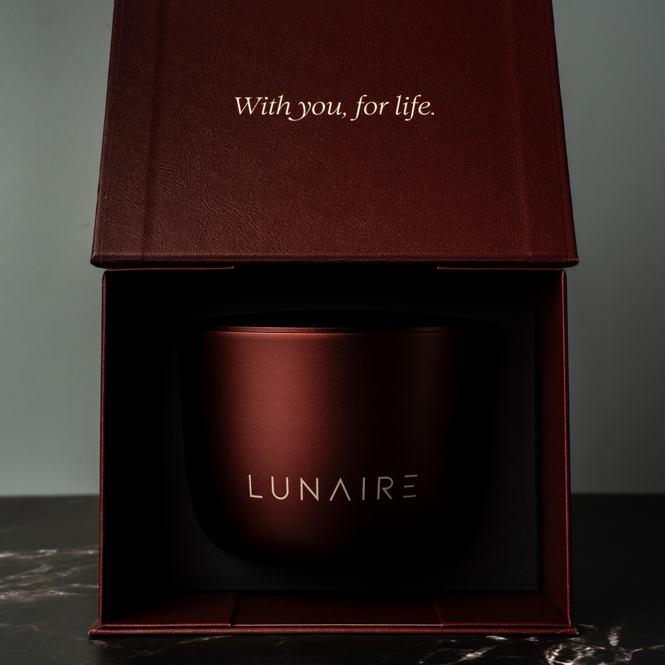 Red aluminium refillable candle jar with 'LUNAIRE' branding in an open box on a dark surface.
