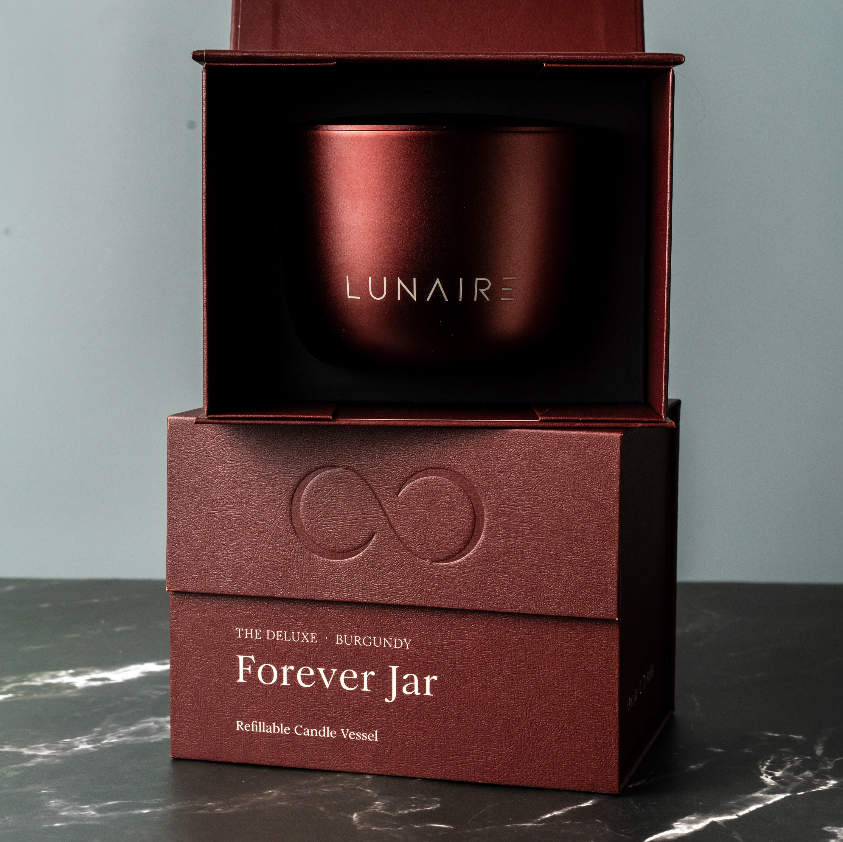Red refillable candle jar with 'LUNAIRE' branding in a matching box on a dark surface.
