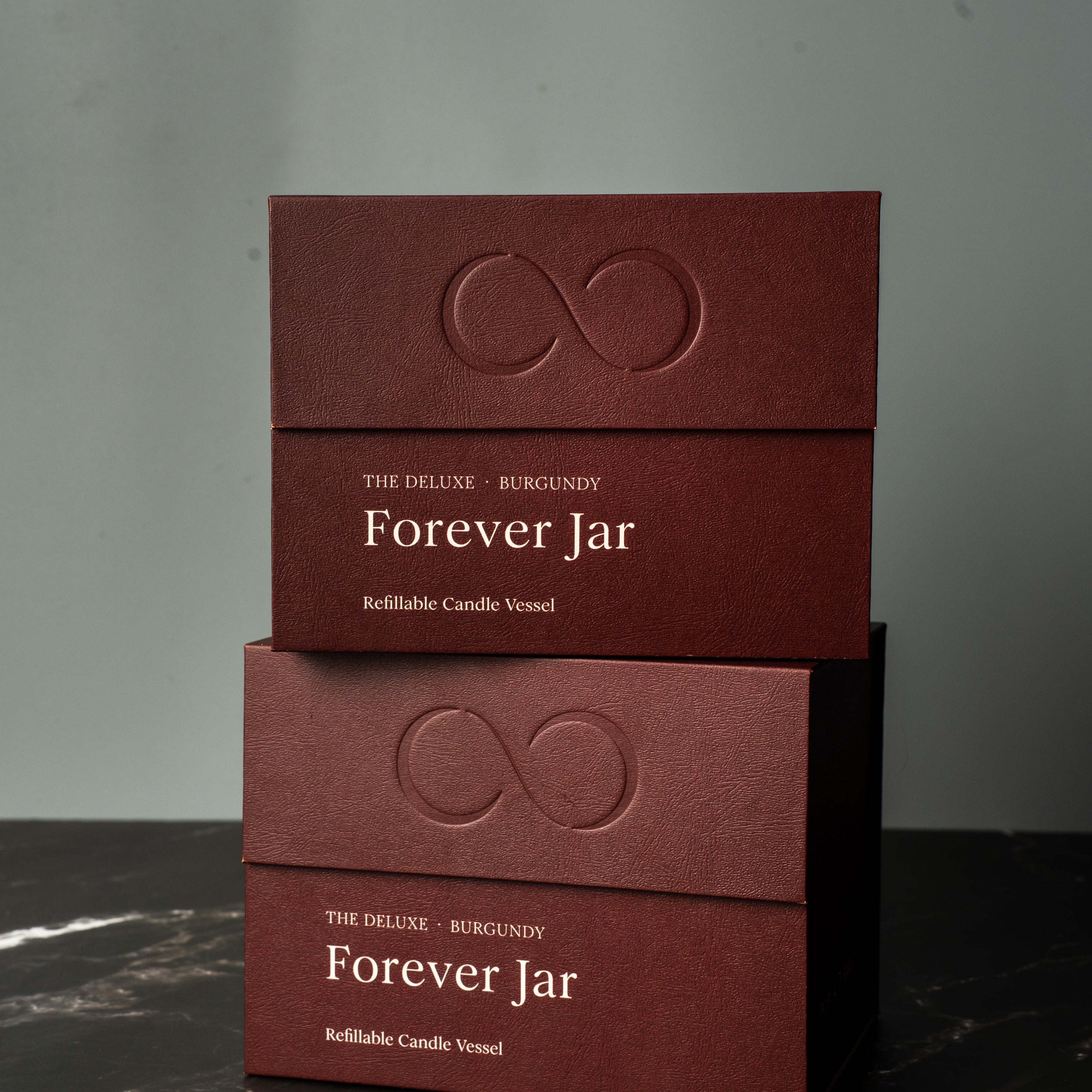 Two burgundy boxes labeled 'Forever Jar' on a dark marble surface with a gray background. Premium Gift Box.