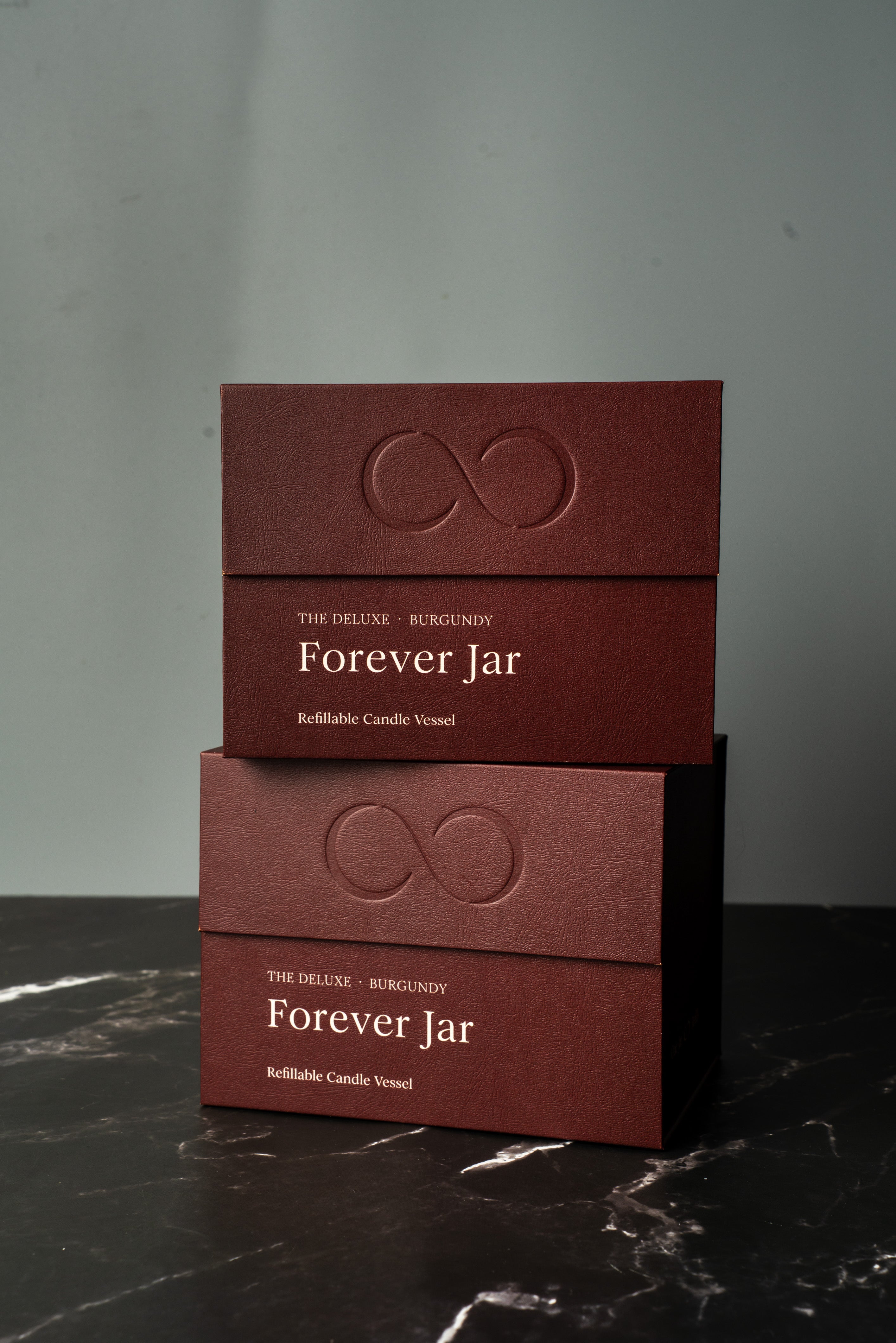 Two burgundy boxes labeled 'Forever Jar' on a dark marble surface with a gray background. Premium Gift Box.