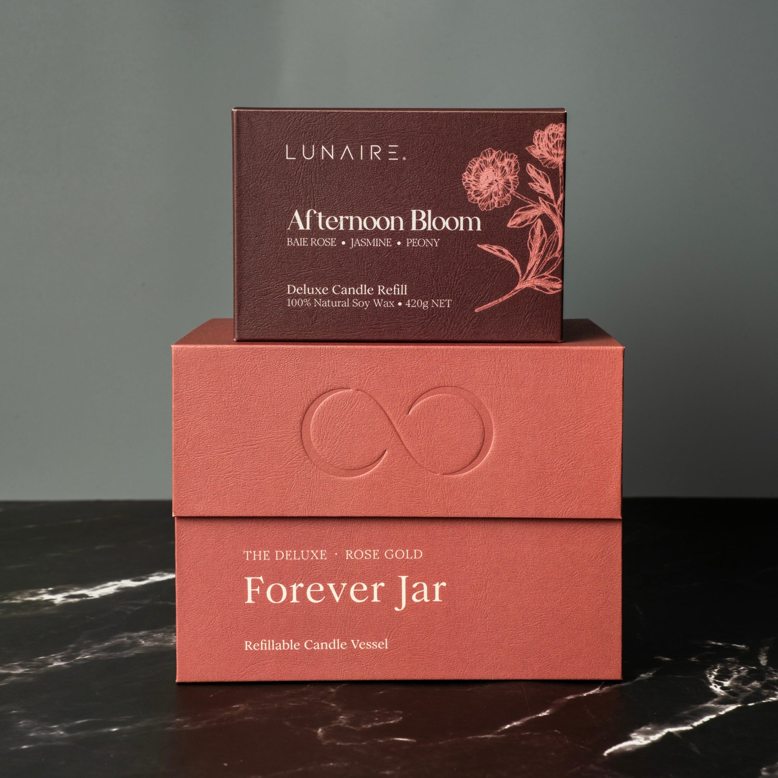 Two boxes, one labeled 'LUNAIRE Afternoon Bloom' and the other 'Forever Jar', on a dark surface with a gray background. Luxury Soy Candle Set