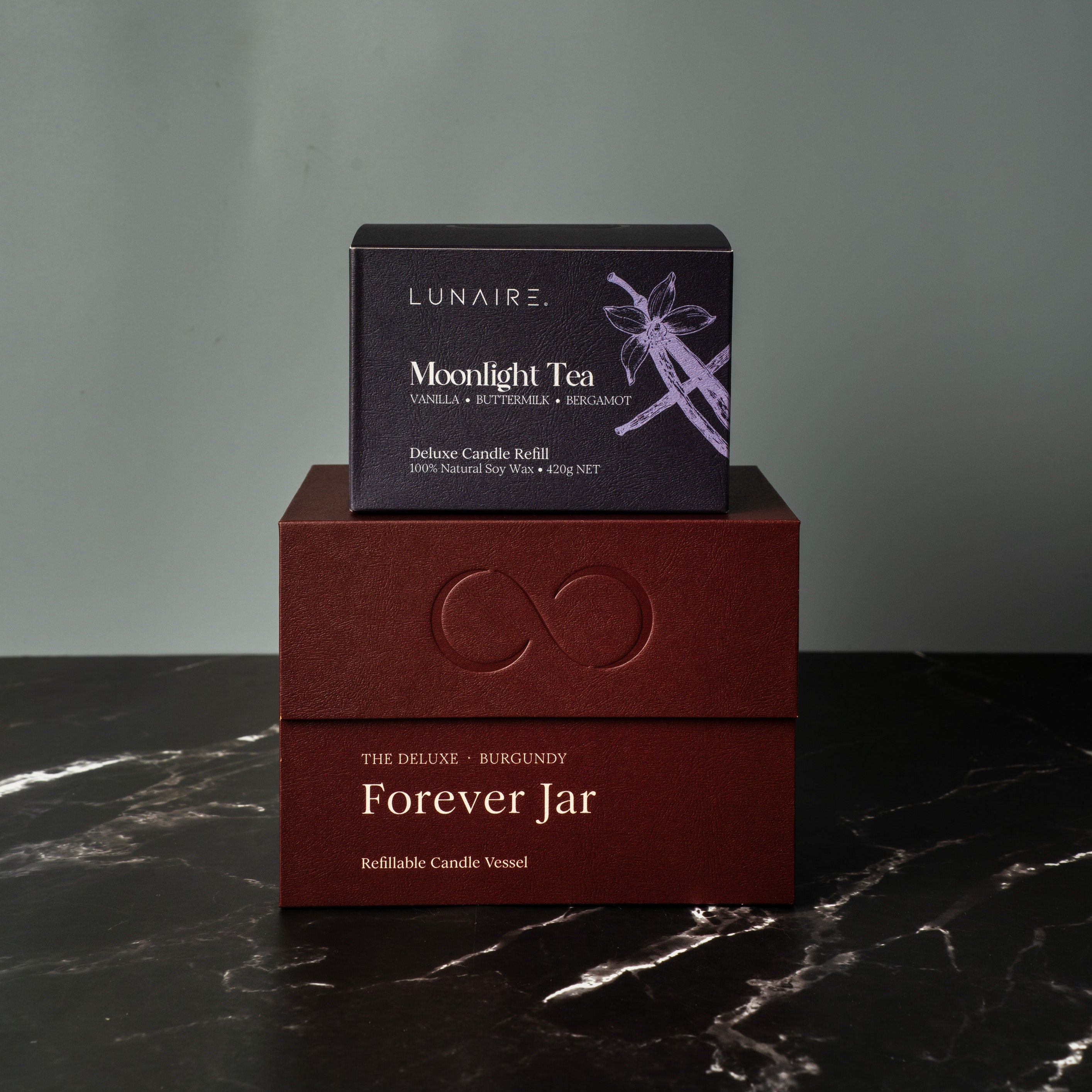 Two boxes, one labeled 'Lunaire' and the other 'Forever Jar', on a dark marble surface with a gray background. Luxury Soy Candle Gift Set.