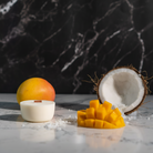 Silver Forever Jar Scented Candle and Coconut Mango Refill on a marbled floor with mango and coconuts surrounding