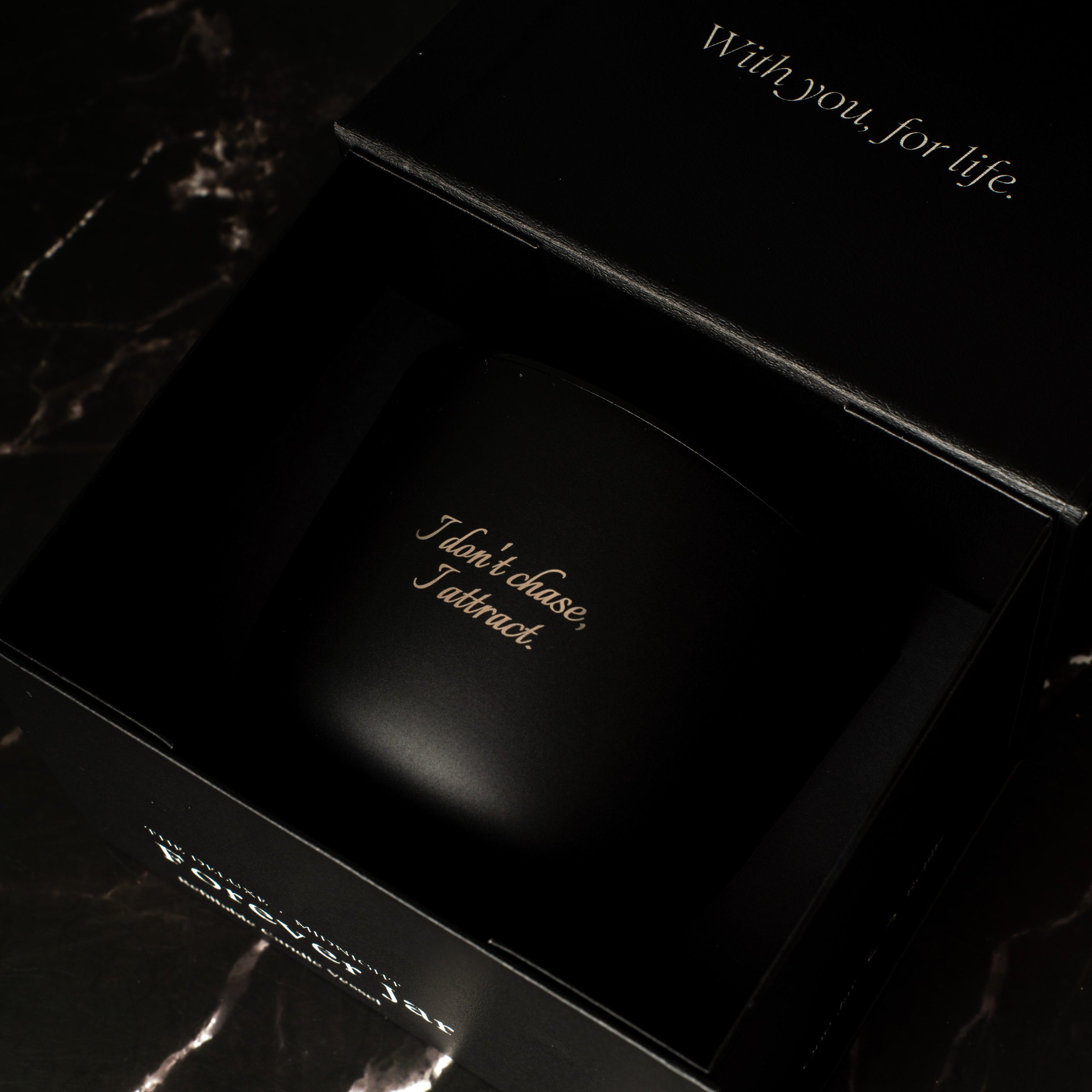 Black candle premium box with engraved text on a dark marble surface