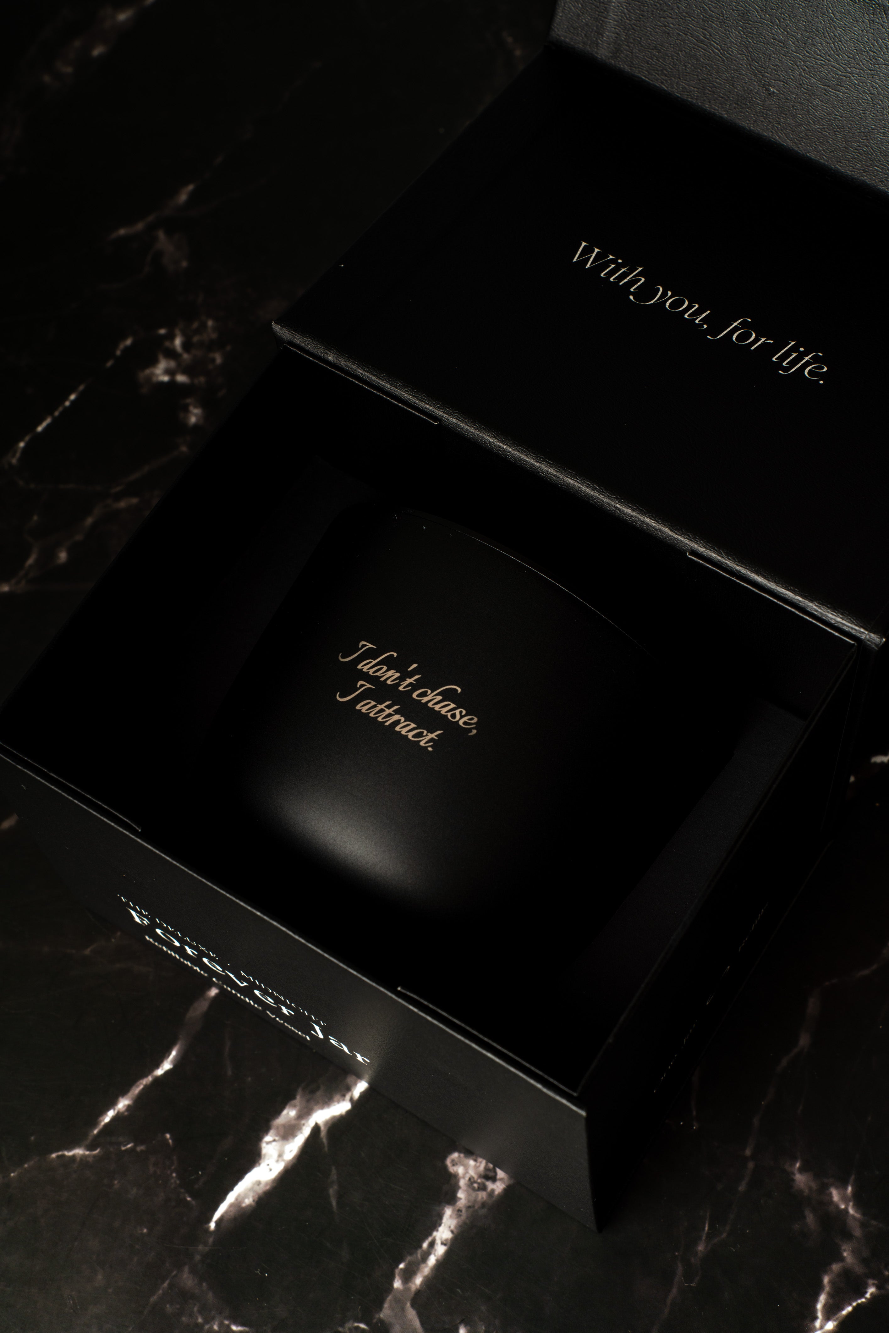Black candle premium box with engraved text on a dark marble surface