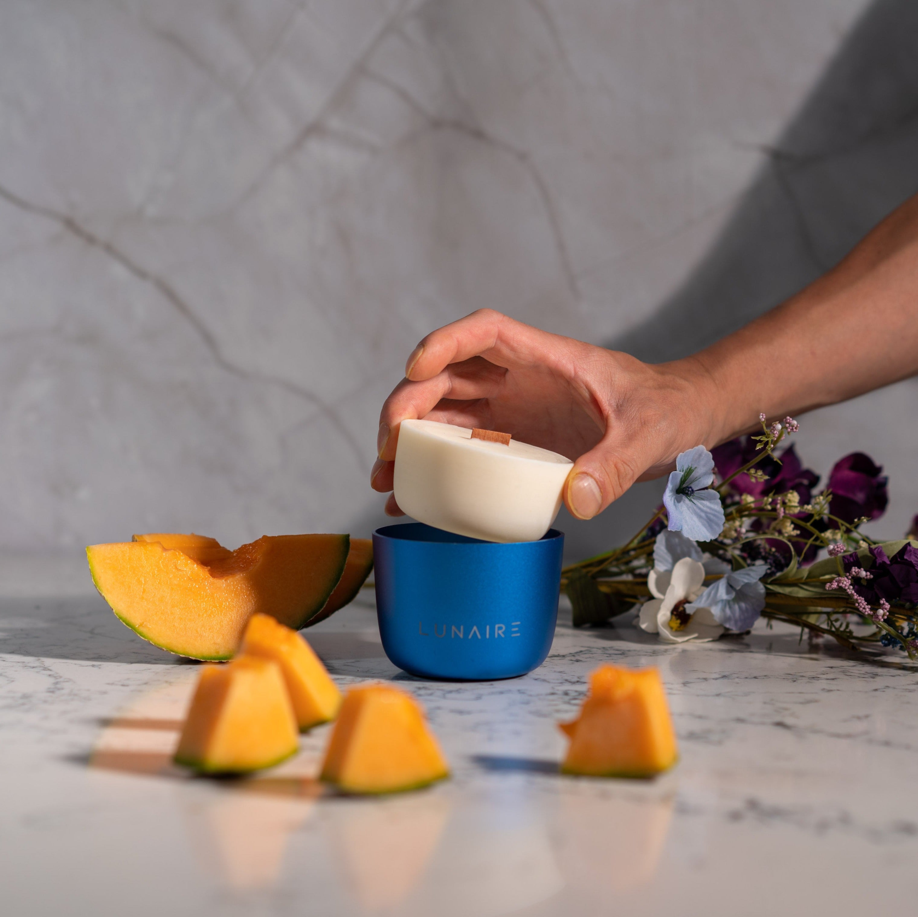 Blue Forever Jar Scented Soy Candle with Melon slices and purple flowers in the background