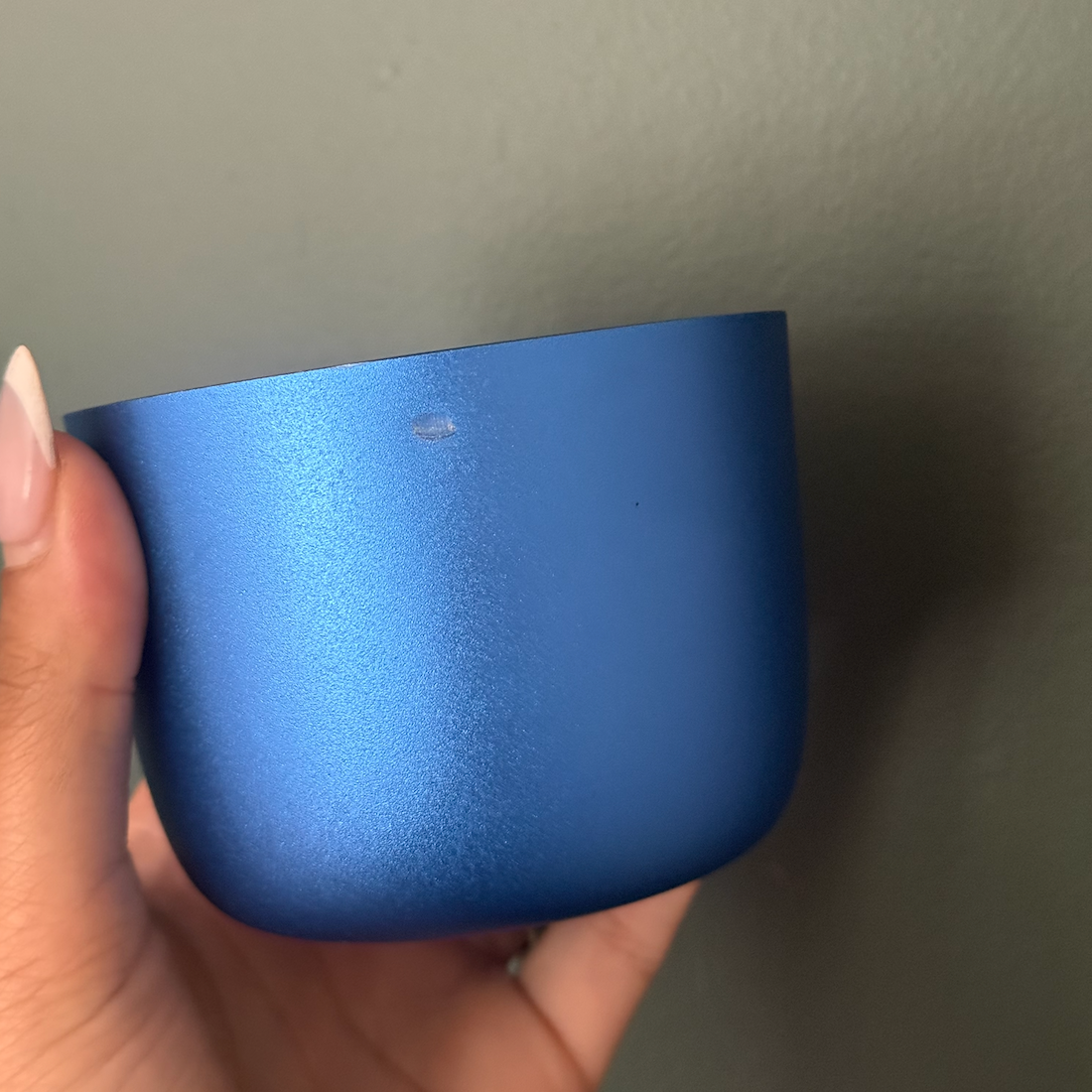 Hand holding a blue candle jar against a plain background