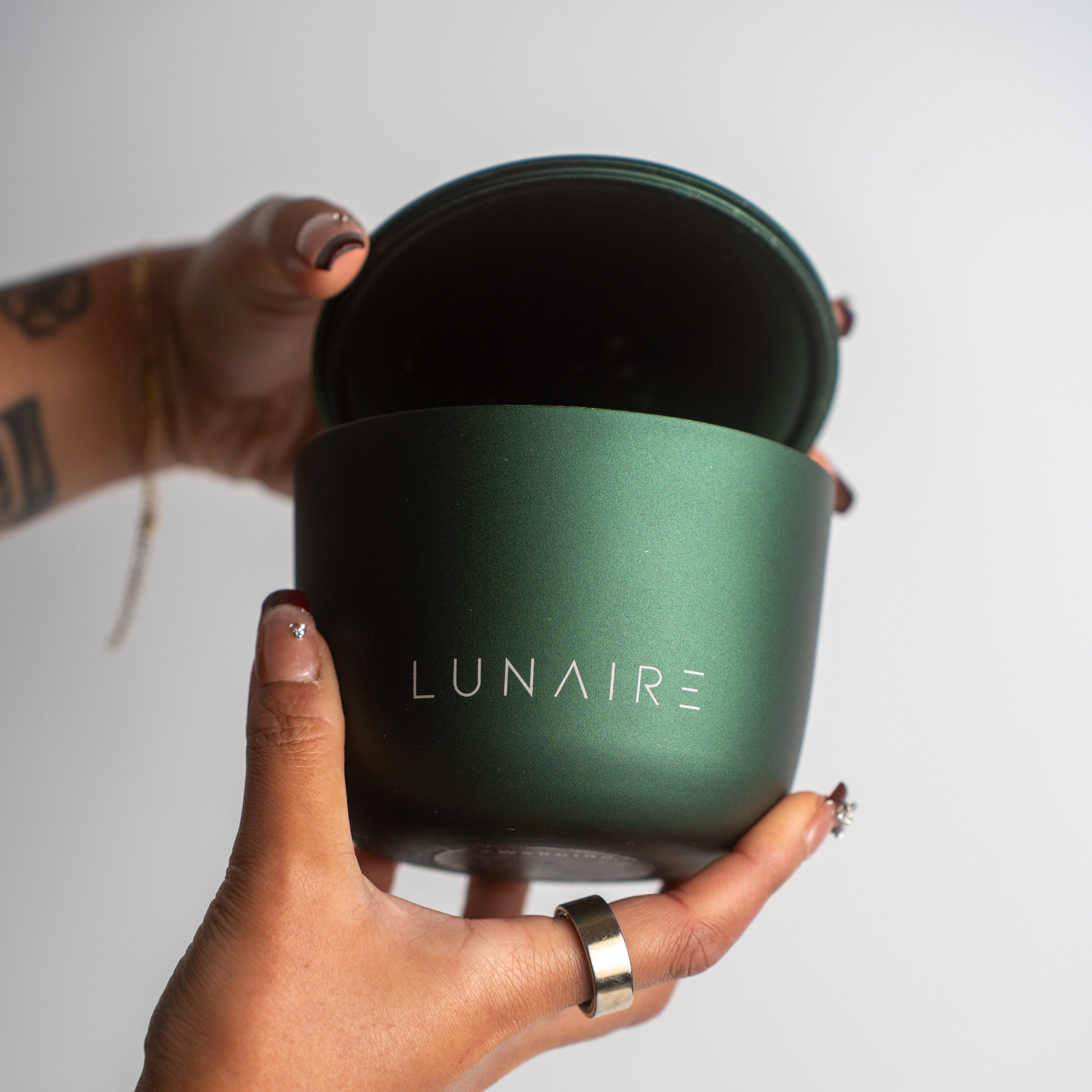 Hand holding a green aluminium luxury candle with 'LUNAIRE' branding against a plain background