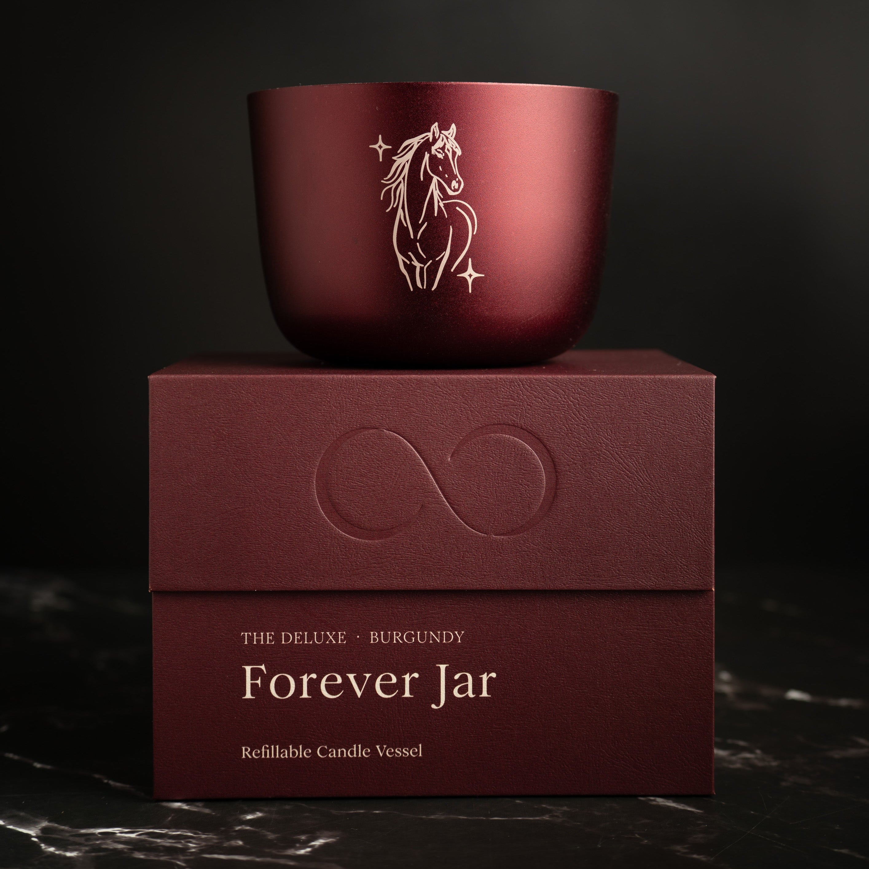 Burgundy candle jar with horse design on a matching box against a dark background