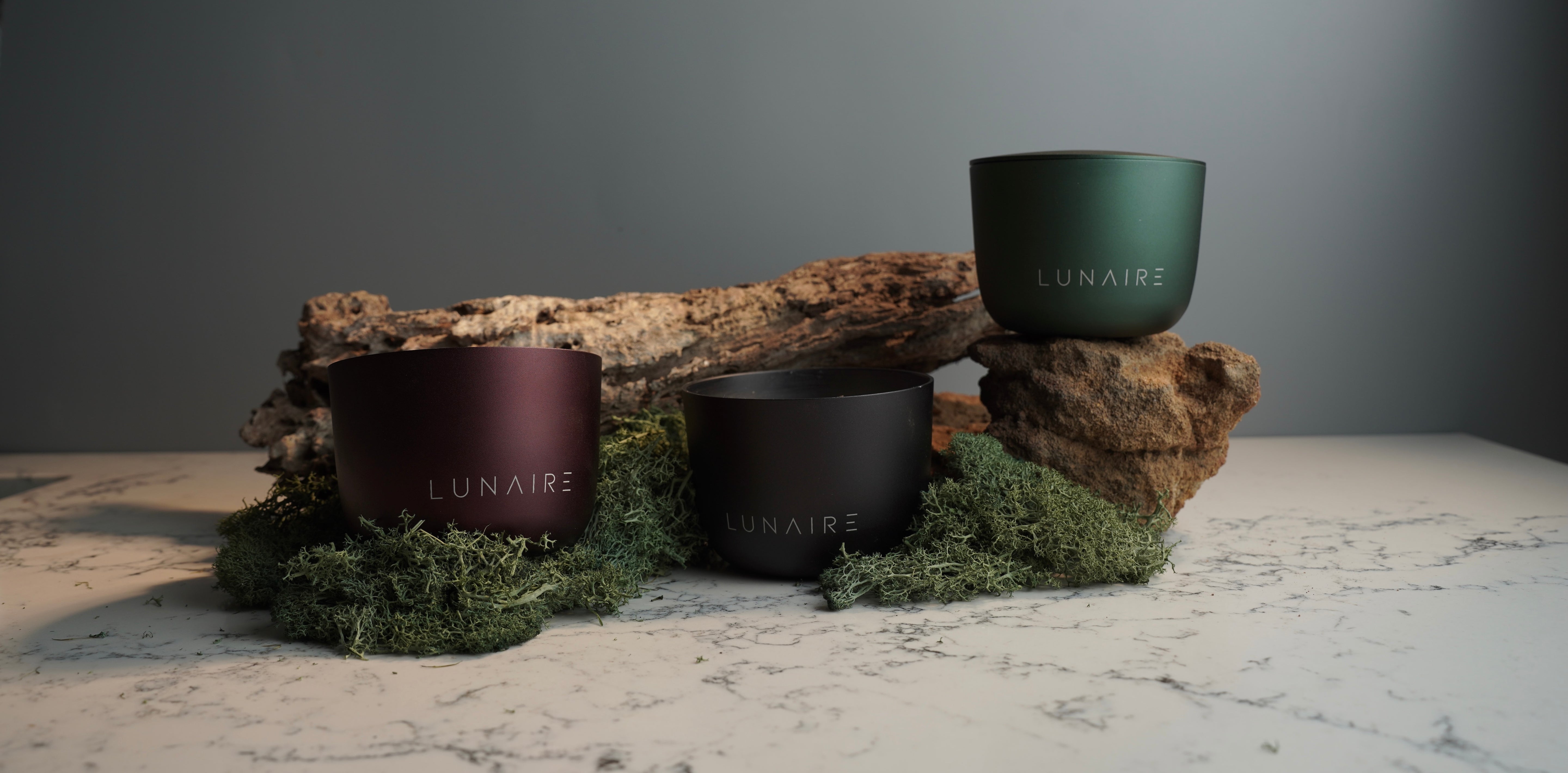 Three 'LUNAIRE' candles on a stone surface with a natural background