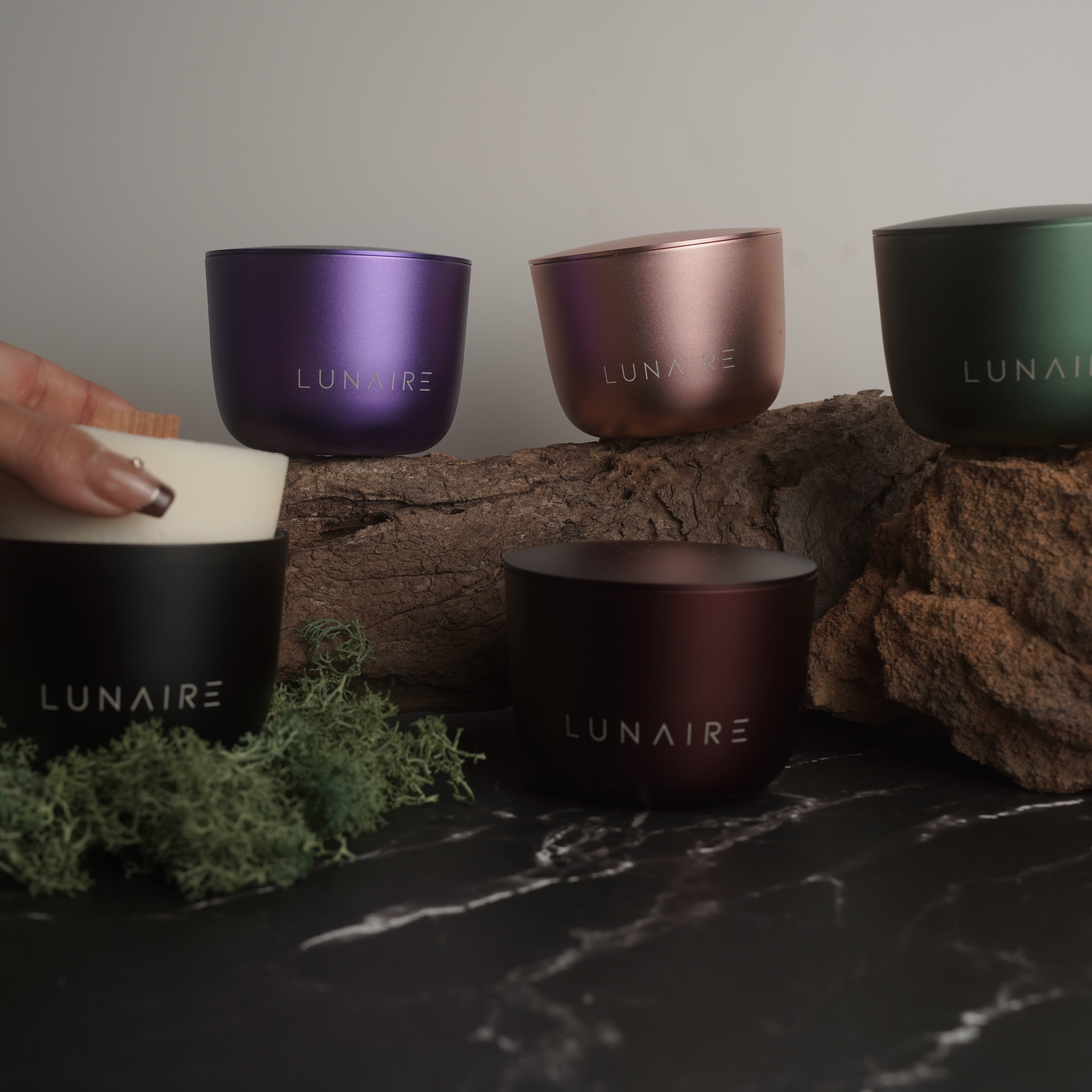 Set of LUNAIRE candles in various colors on a stone surface with a hand holding a candle refill.