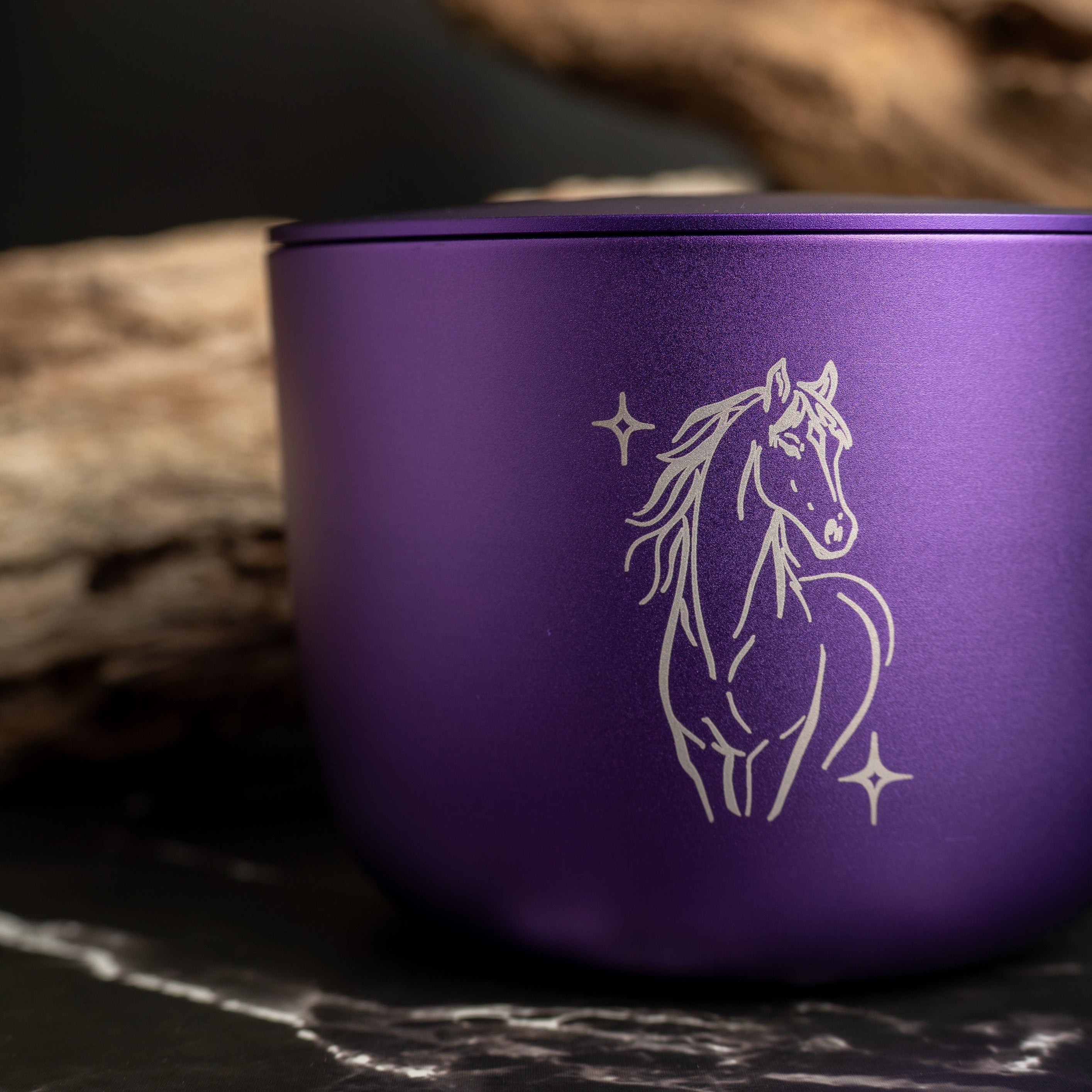 Purple aluminium candle with a horse design on a dark surface