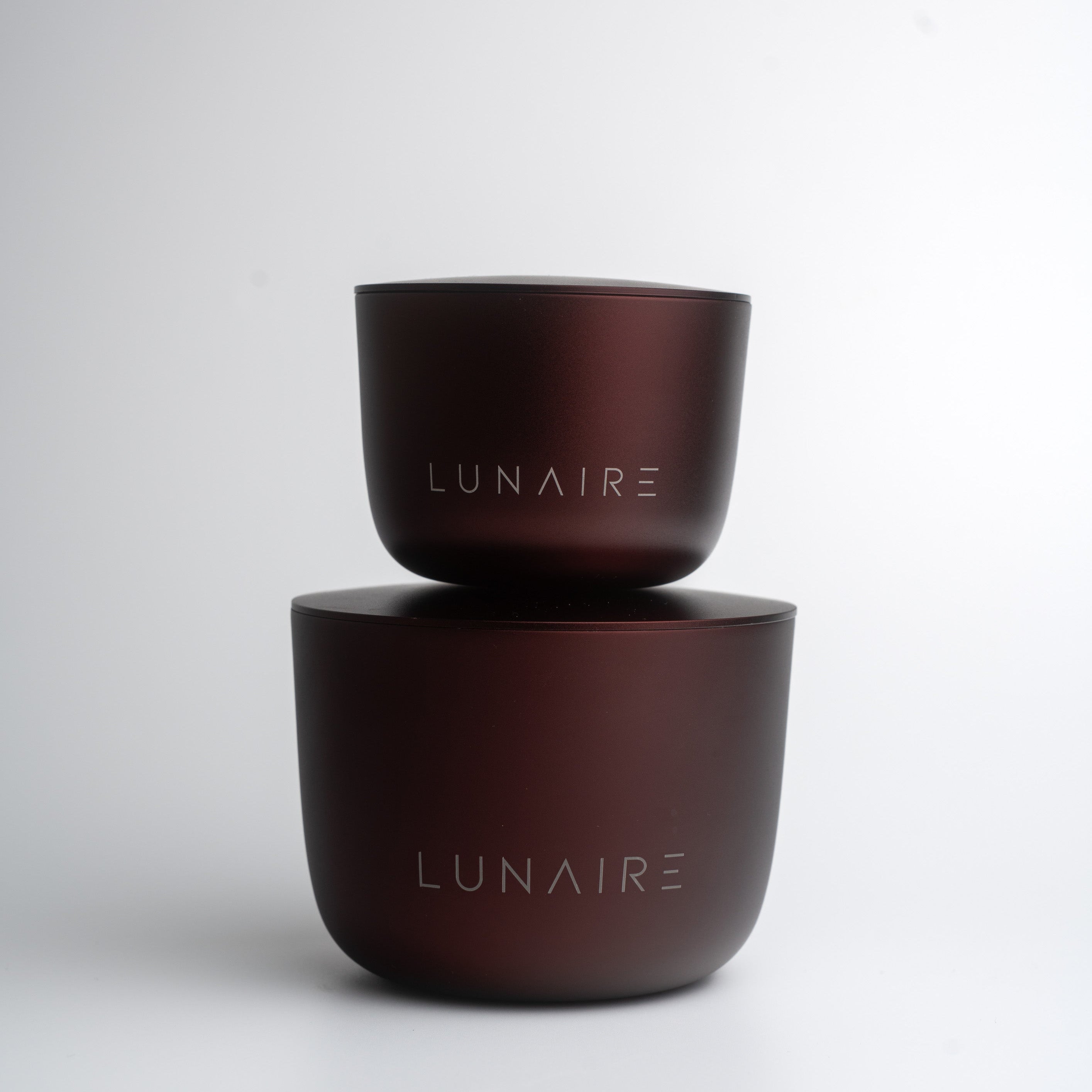 Two burgundy aluminium candle containers with 'LUNAIRE' branding on a white background