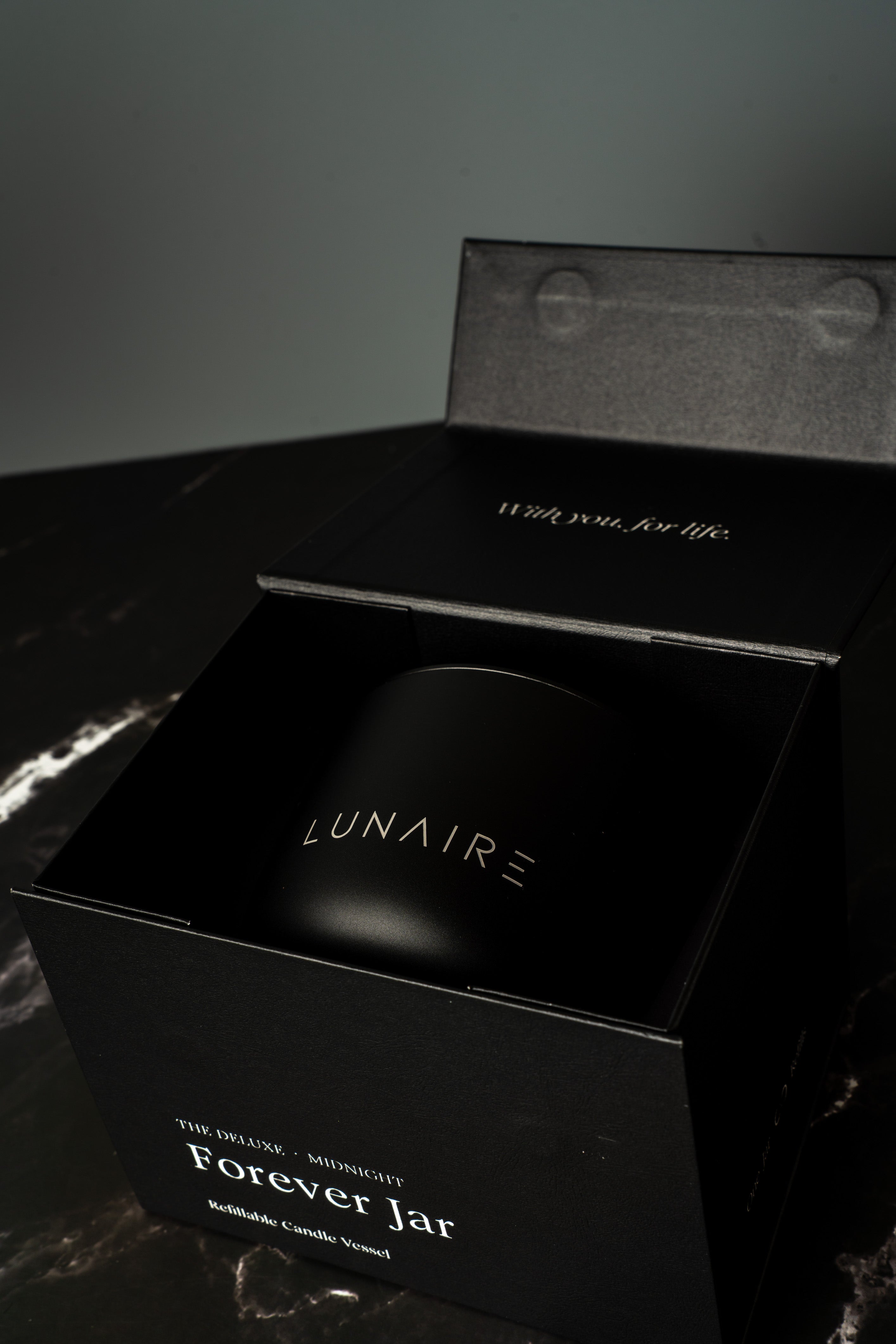 Black gift box with 'LUNAIRE' branding on a marble surface holding an aluminium candle vessel.