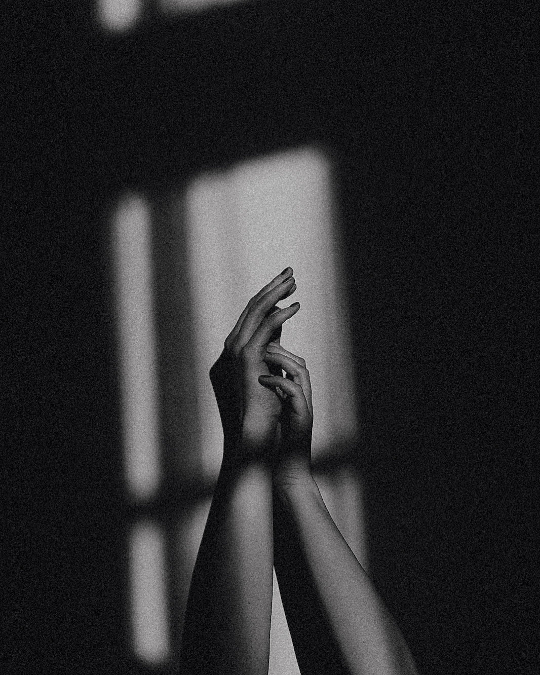 Black and white photo of hands reaching towards a light source casting shadows.