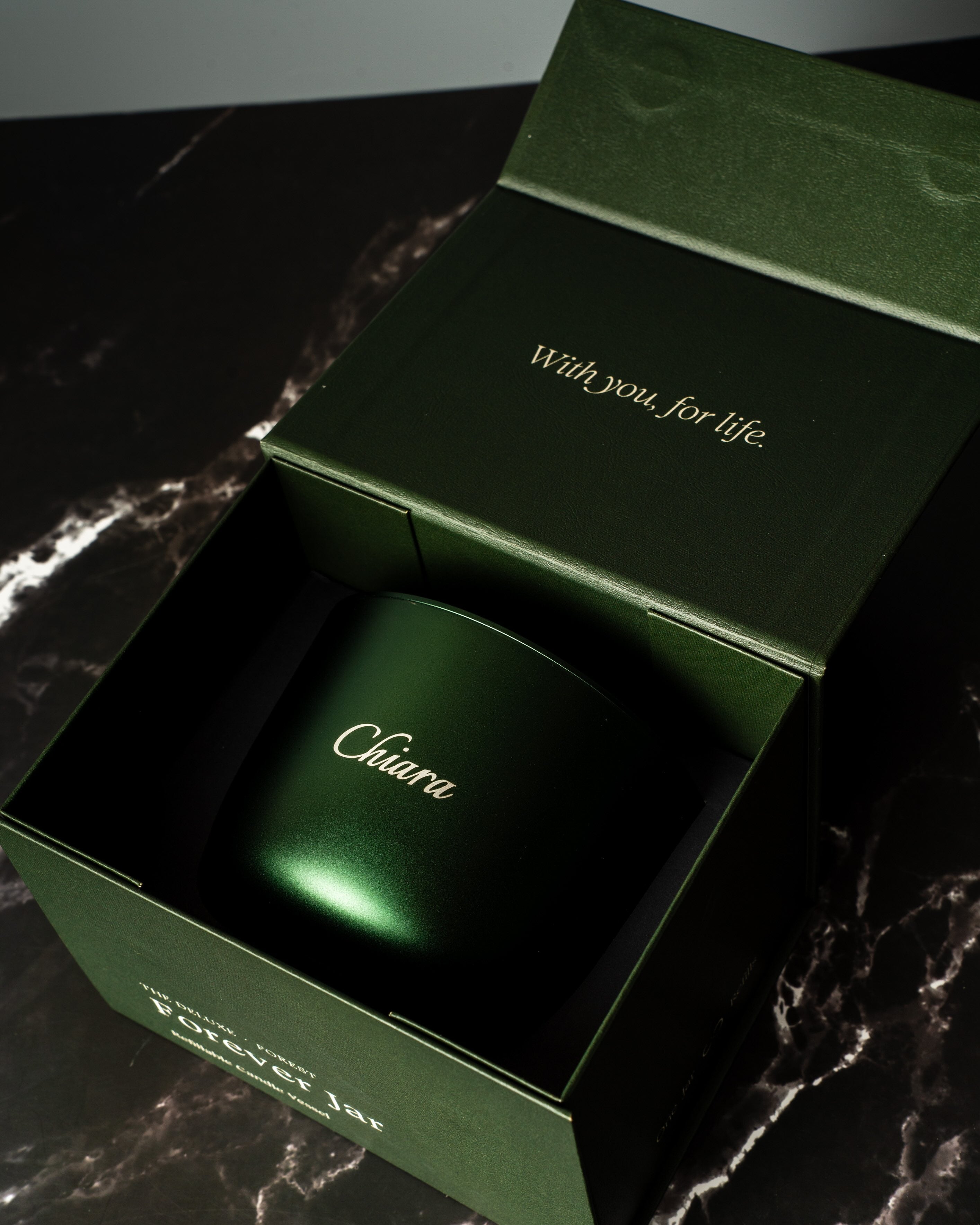 forest green forever candle with engraving 'Chiara' opened on a marbled bench top