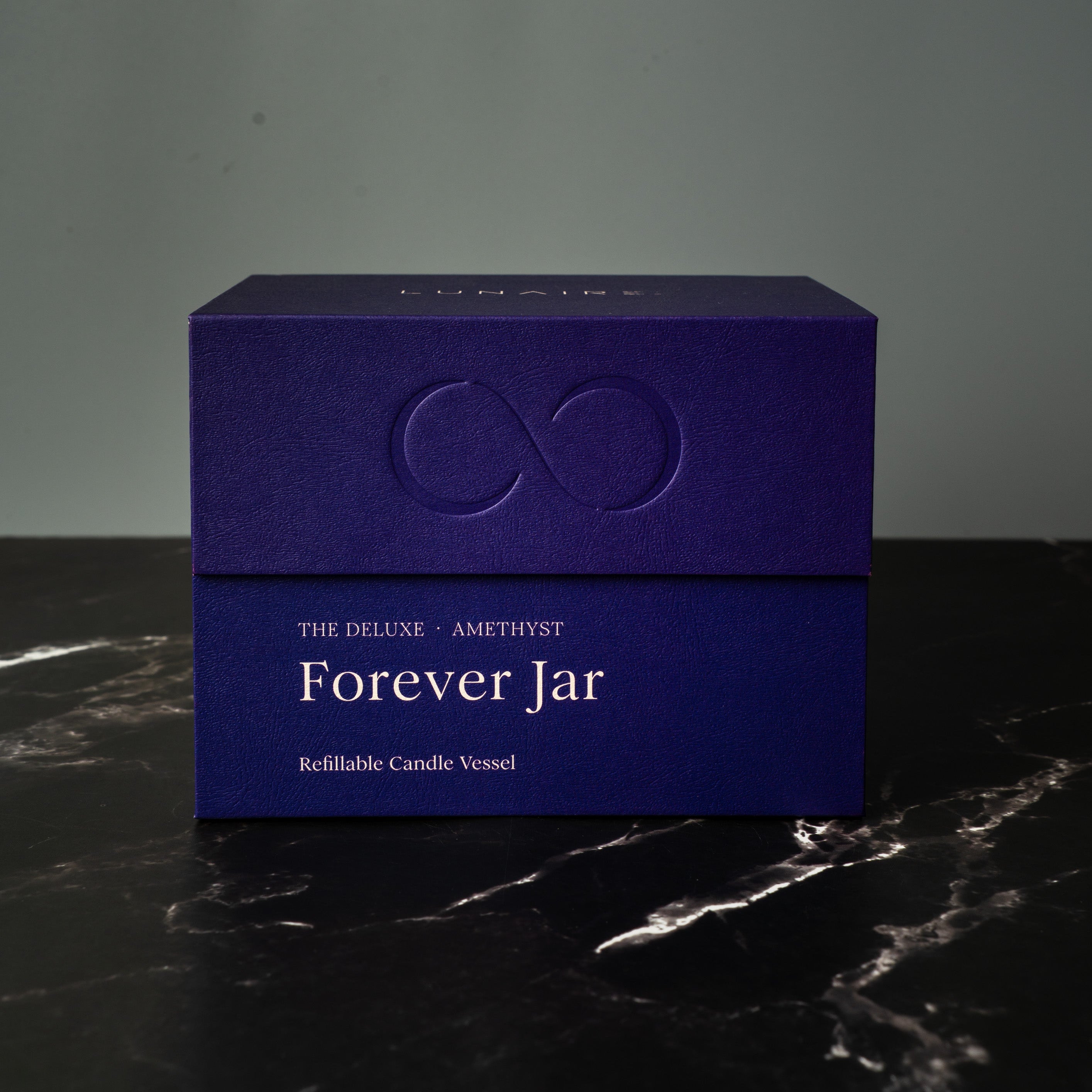 Purple premium gift box labeled 'Forever Jar' on a dark surface with a gray background. Refillable Aluminium Candle