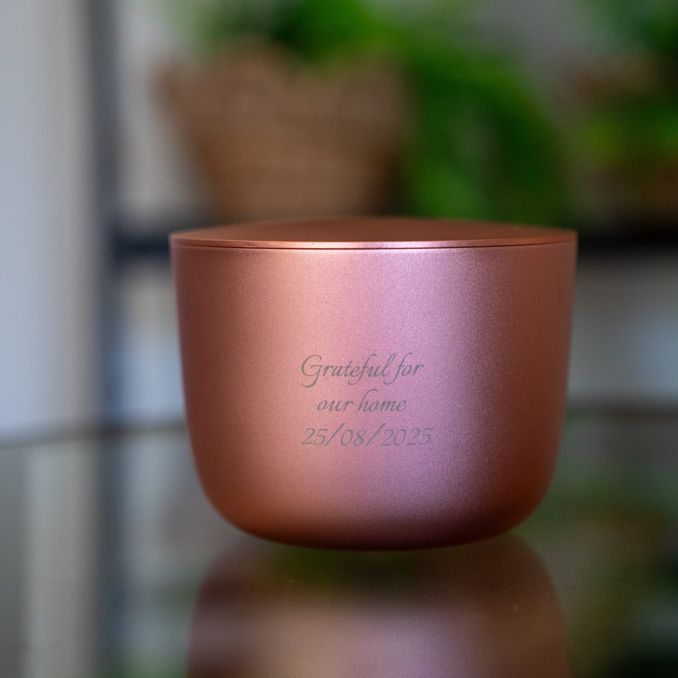 Rose gold luxury candle with engraved text on a reflective surface with a blurred background