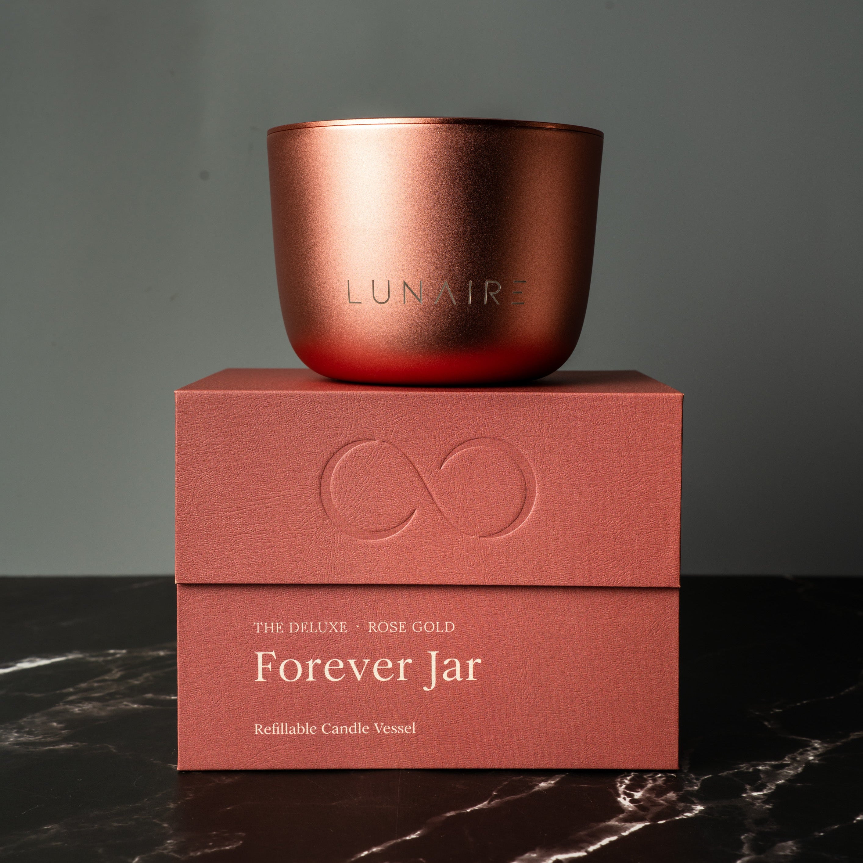 Rose Gold-colored aluminium candle jar on a premium gift box with 'LUNAIRE' branding on a dark surface. Lunaire Refillable Aluminium Candles.