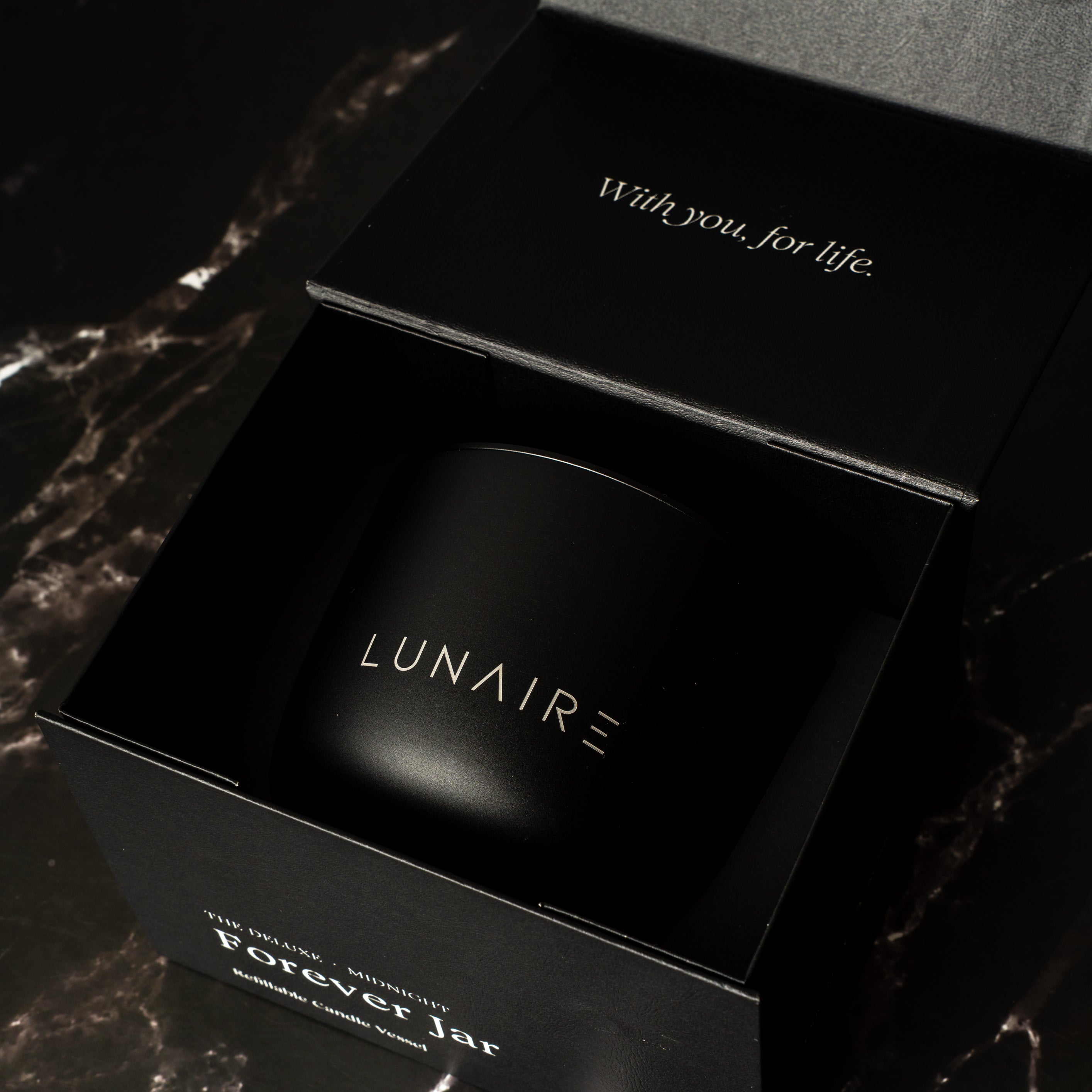 Black premium gift box with 'LUNAIRE' branding on a dark marble surface holding a refillable aluminium candle.