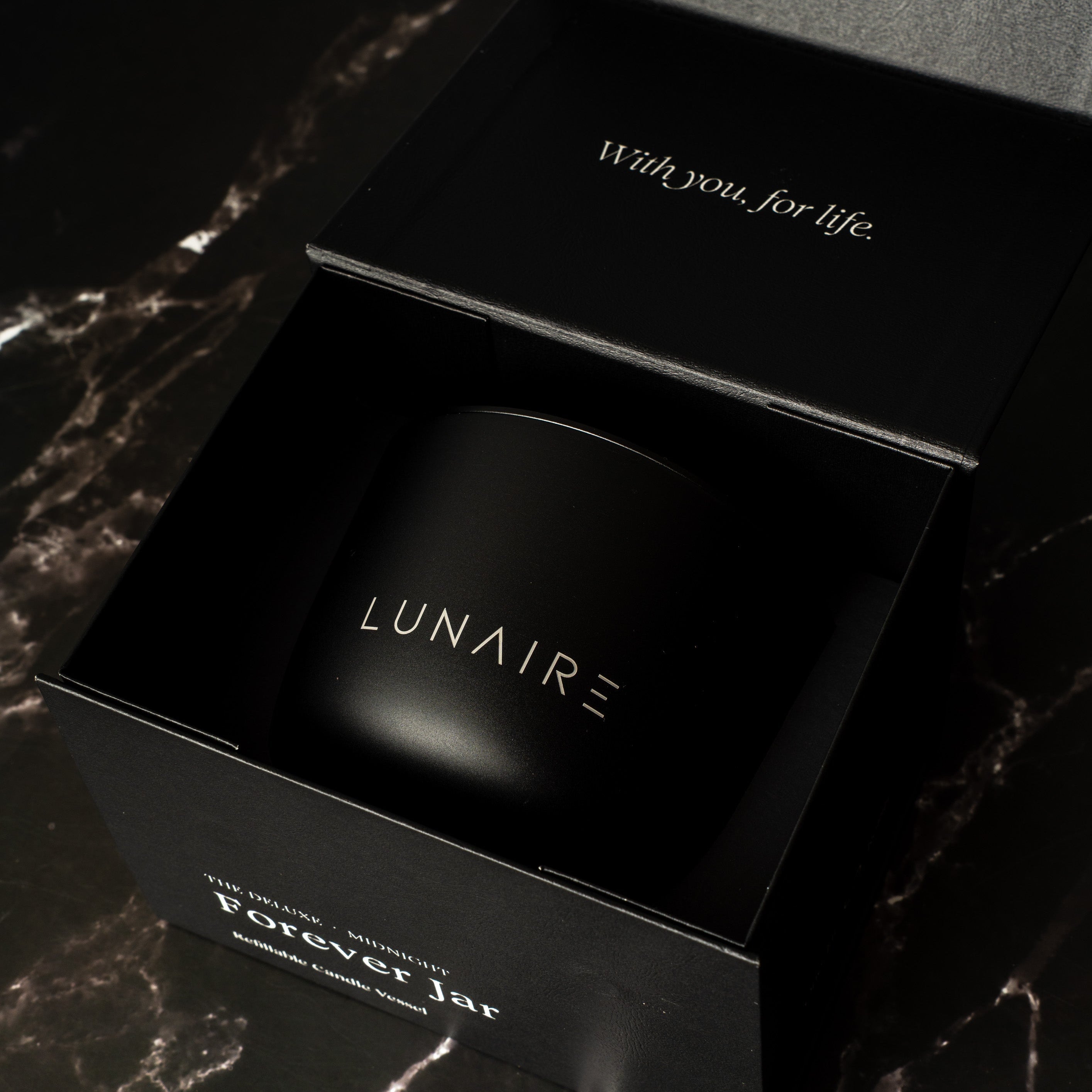 Black premium gift box with 'LUNAIRE' branding on a dark marble surface holding a refillable aluminium candle.