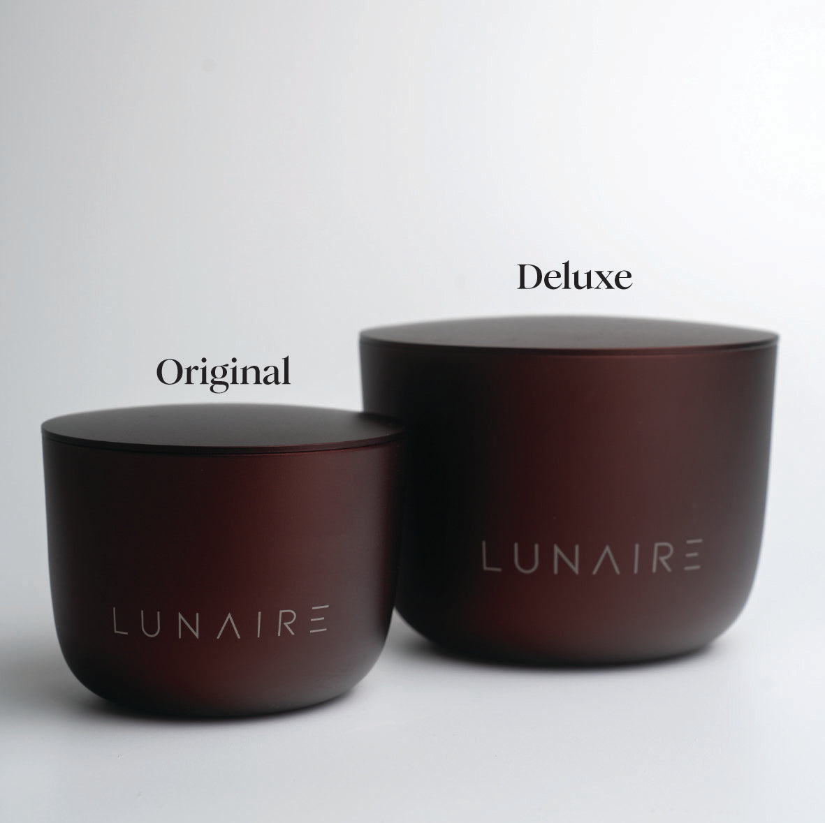 Two burgundy aluminium candles labeled 'Original' and 'Deluxe' by LUNAIRE on a light gray background.