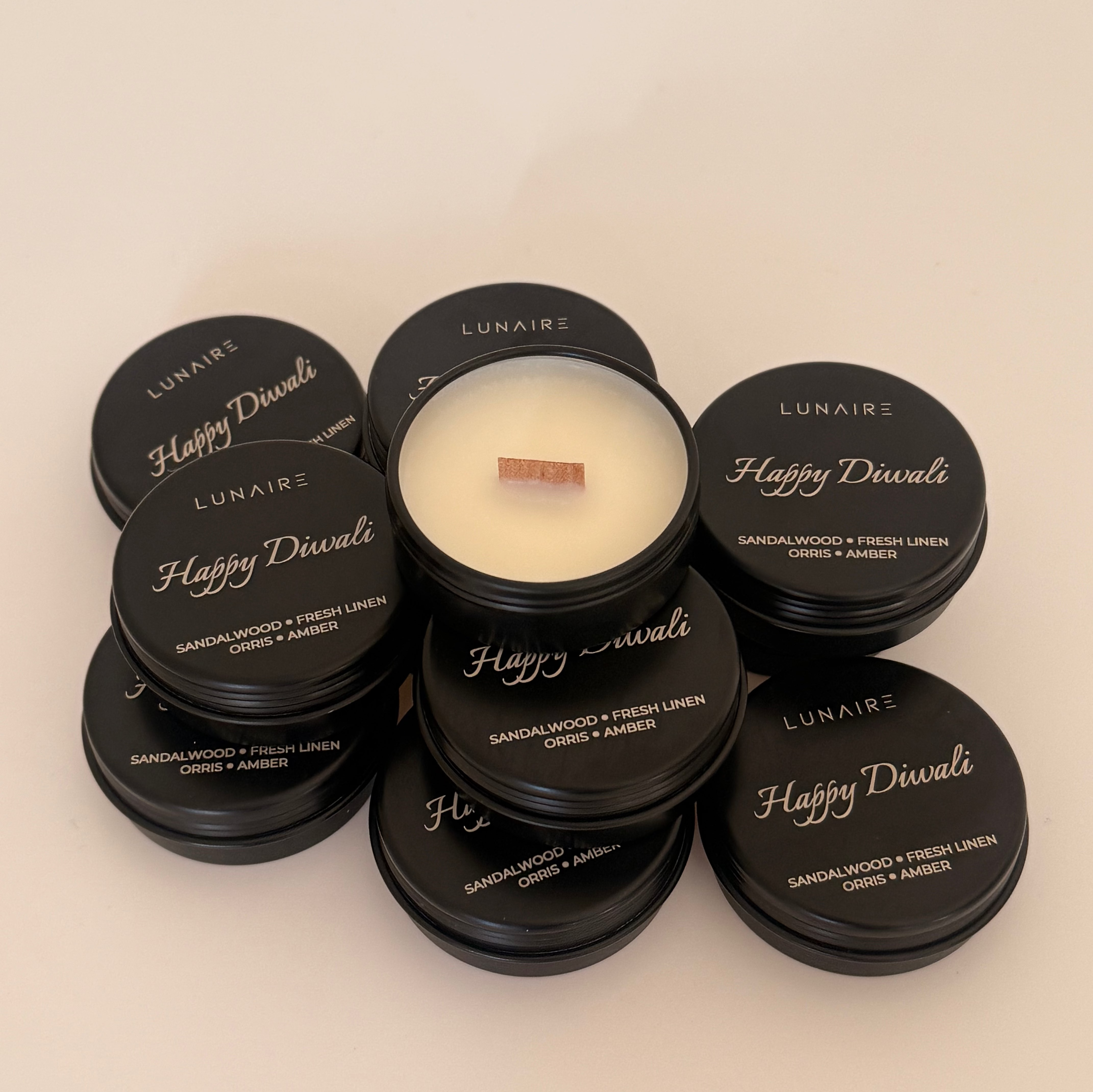Candle with black lids labeled 'Happy Diwali' and 'Lunaire' on a beige background