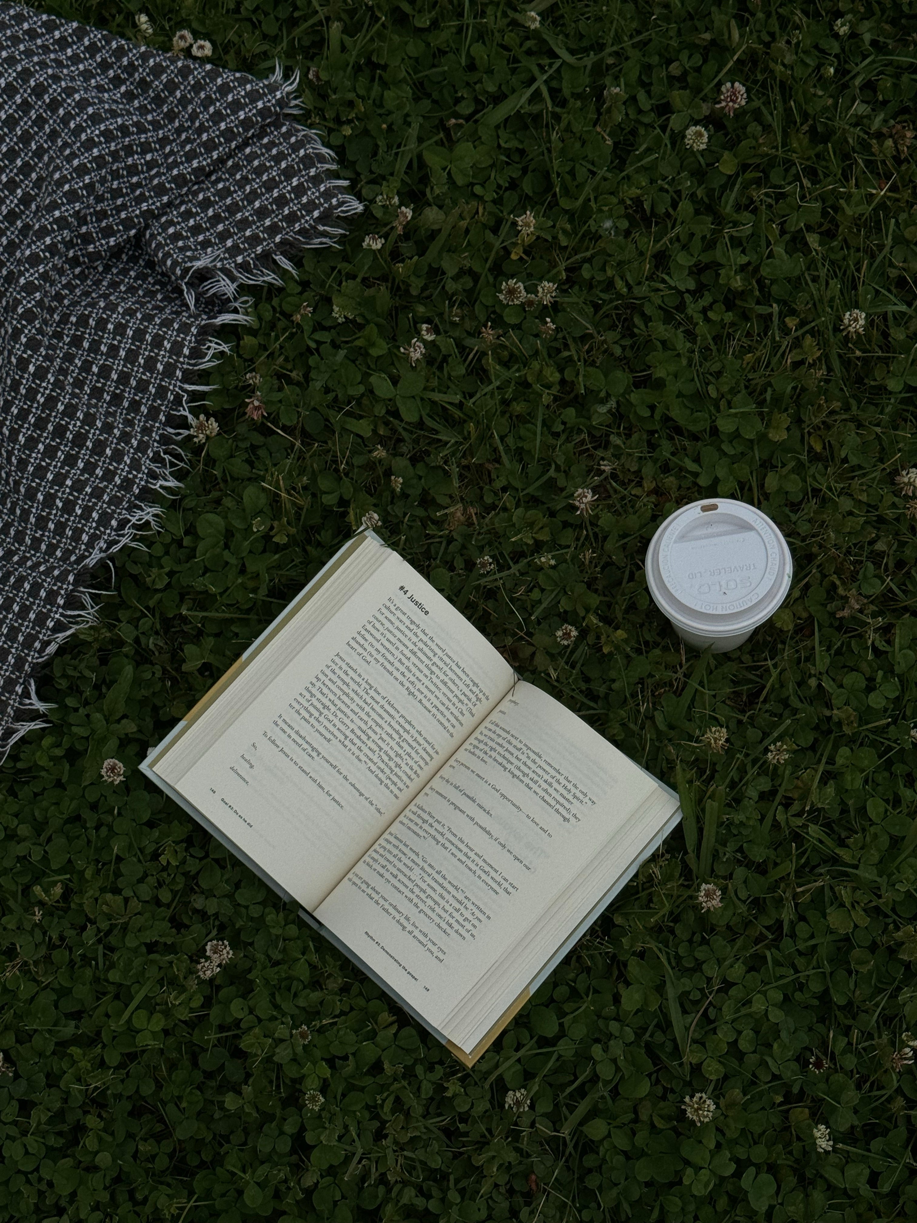 Open book and a coffee cup on grass