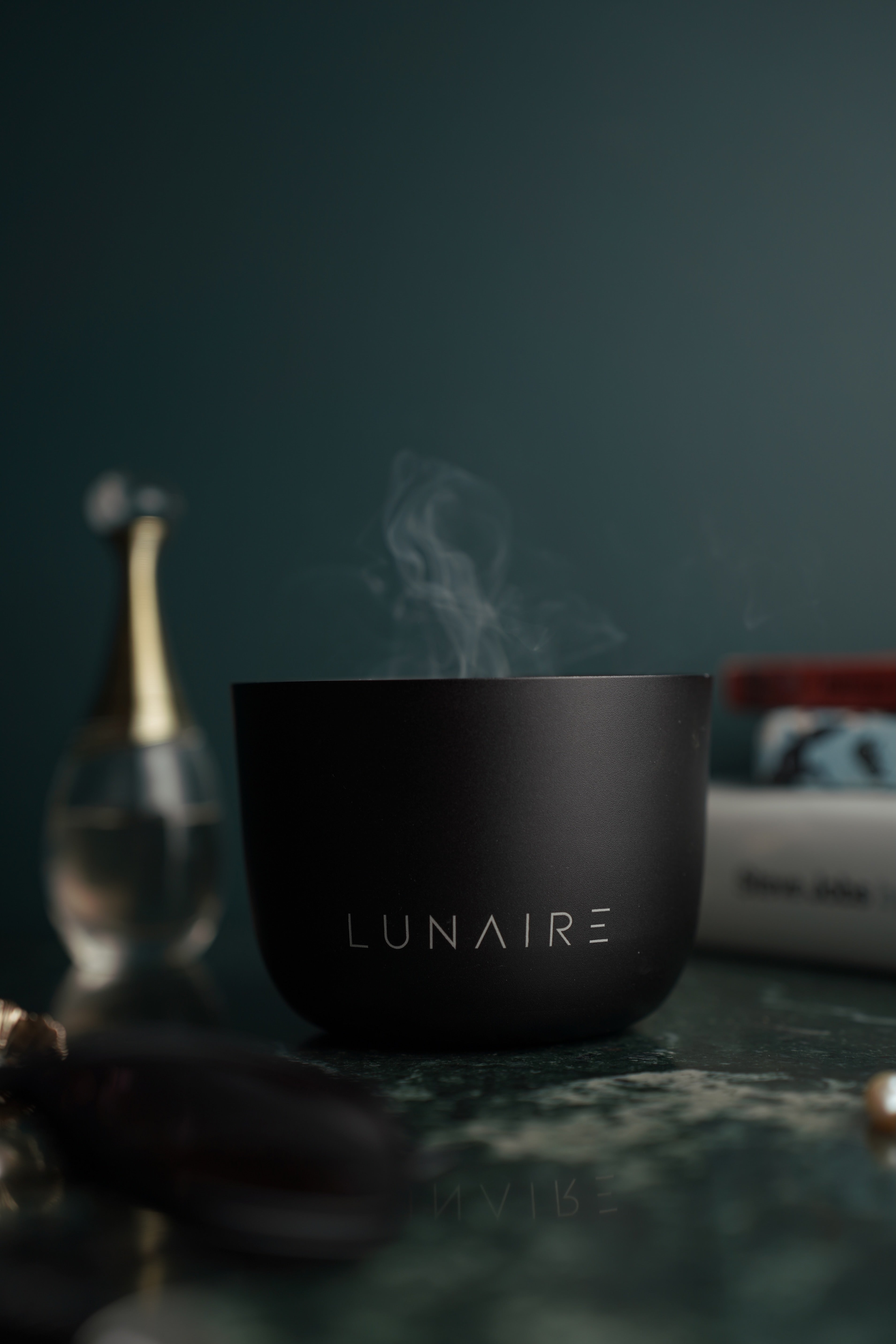 Black 'LUNAIRE' Forever Candle with steam on a dark background