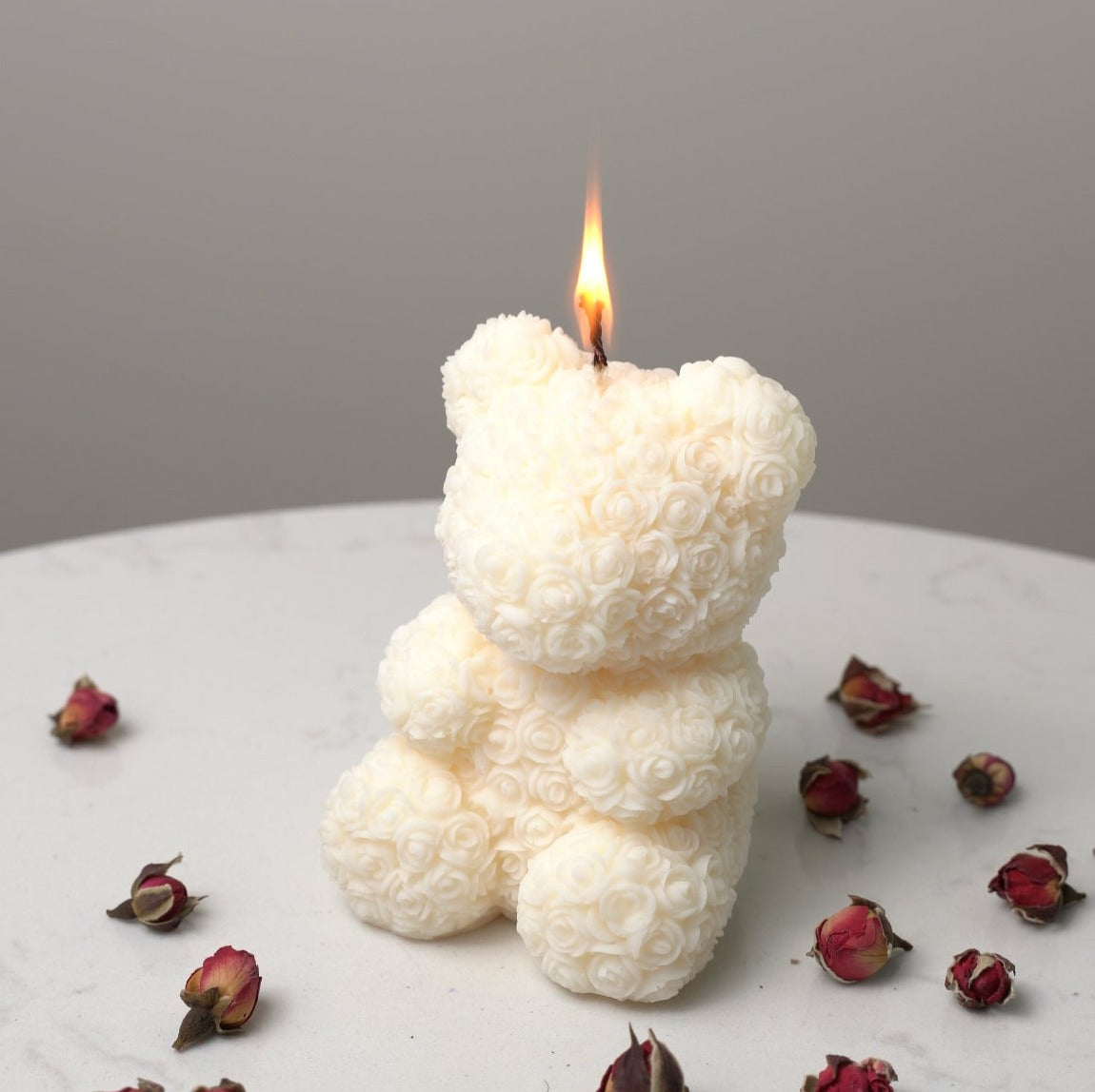 Bear Shaped Decorative Candle with intricate rose pattern lit on a surface covered in dried roses.