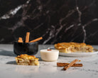 Baked Apple Pie candle Refill on a marbled bench top surrounded by a pie, cinnamon sticks and a mortar.