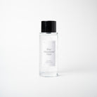 A clear glass bottle of Blue Mountain Mist room spray with a black cap and a white label, centered against a light gray background.