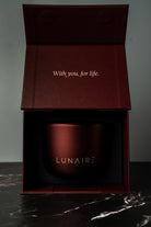 Red aluminium refillable candle jar with 'LUNAIRE' branding in an open box on a dark surface.