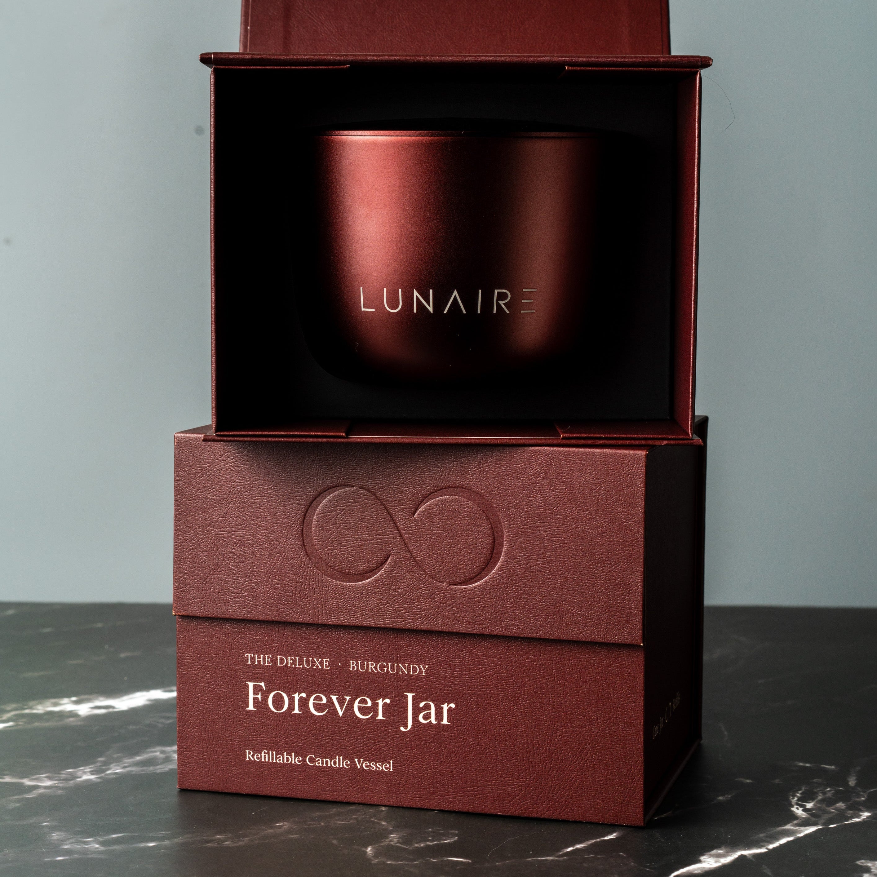 Red refillable candle jar with 'LUNAIRE' branding in a matching box on a dark surface.