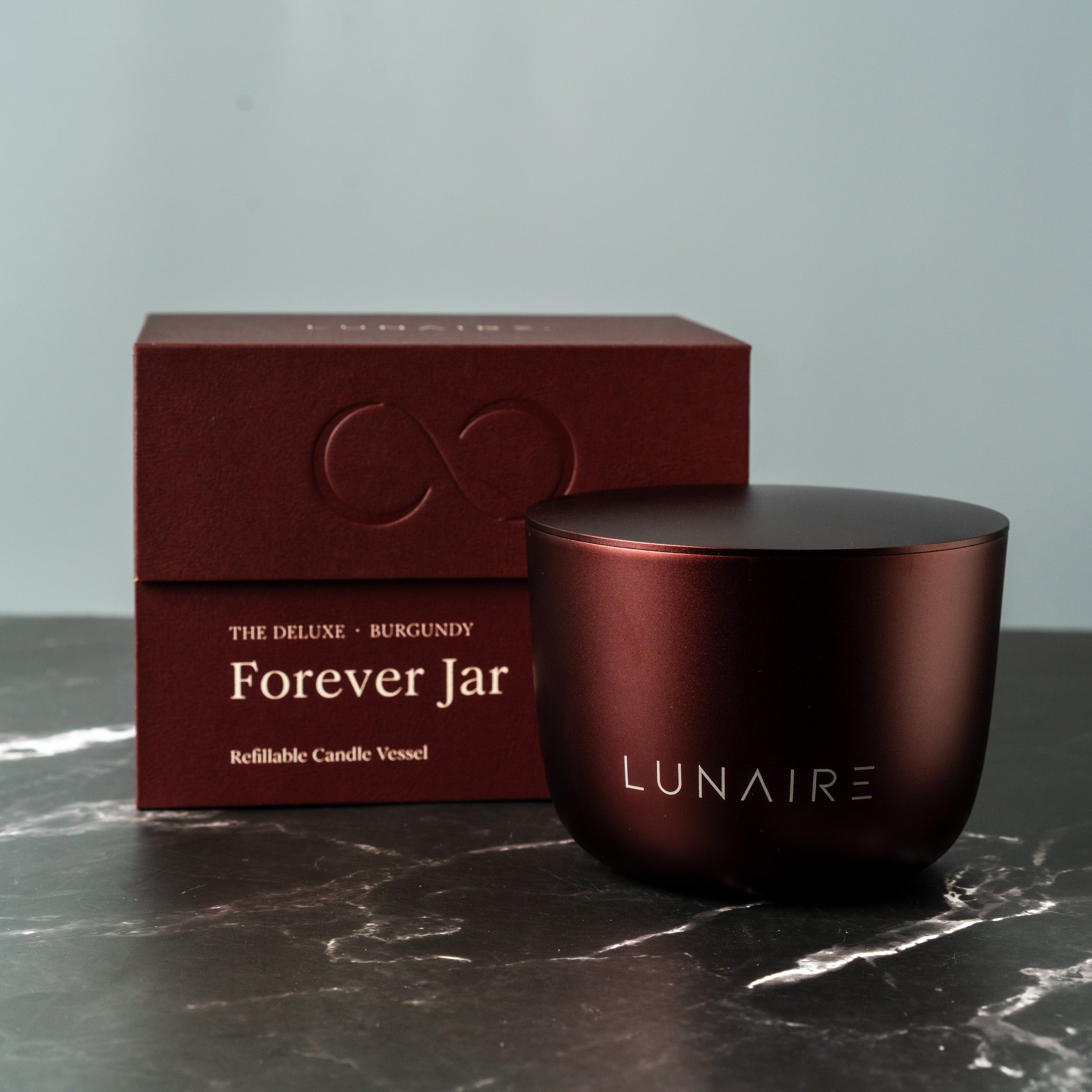 Burgundy refillable candle and box with 'LUNAIRE' branding on a dark surface.