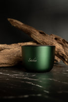 Green aluminium candle with 'Sasha' branding on a dark surface with wooden elements.