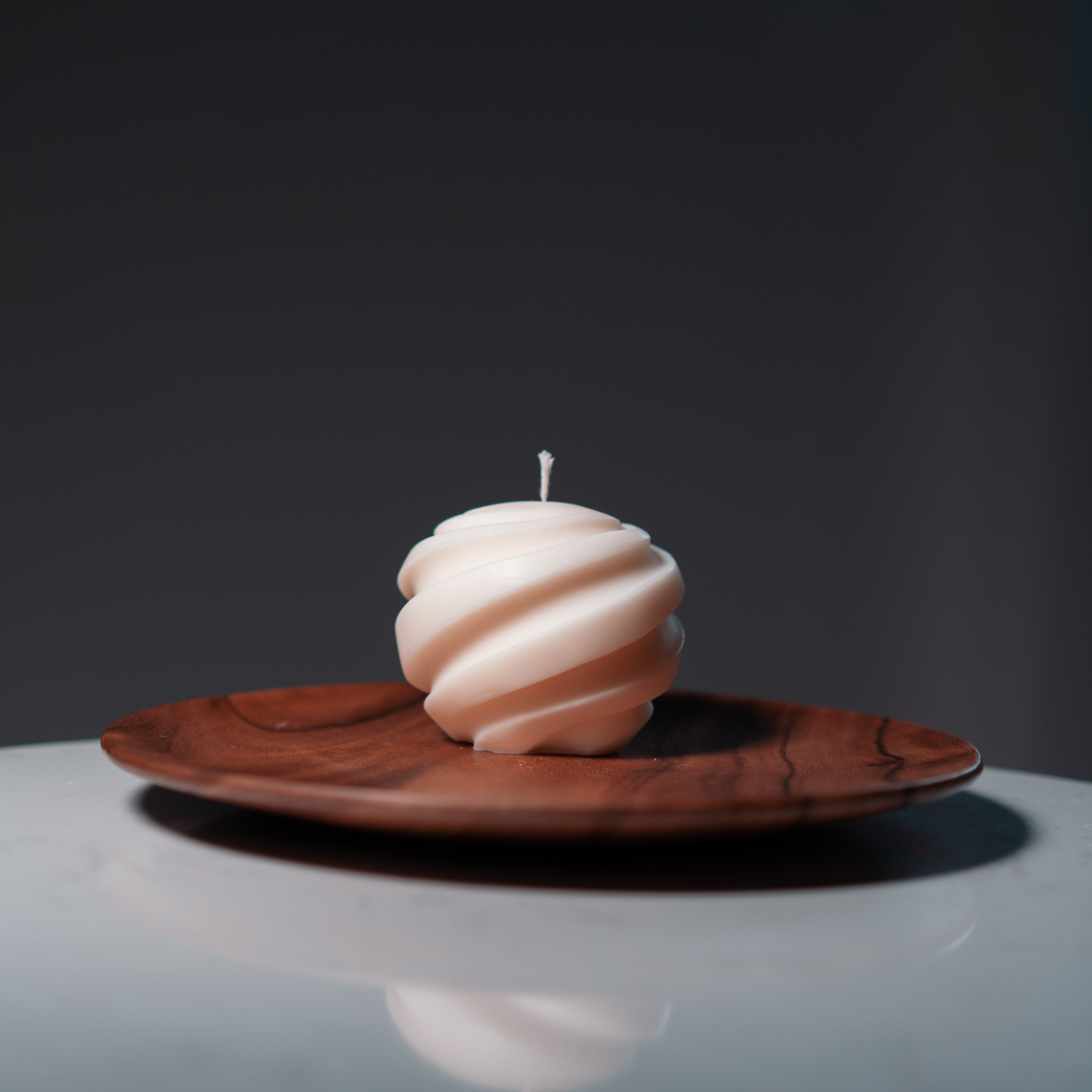 Ball Decorative Candle with cotton wick on a round wooden plate.