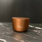 Bronze-colored candle with 'Dani' branding on a dark marble surface