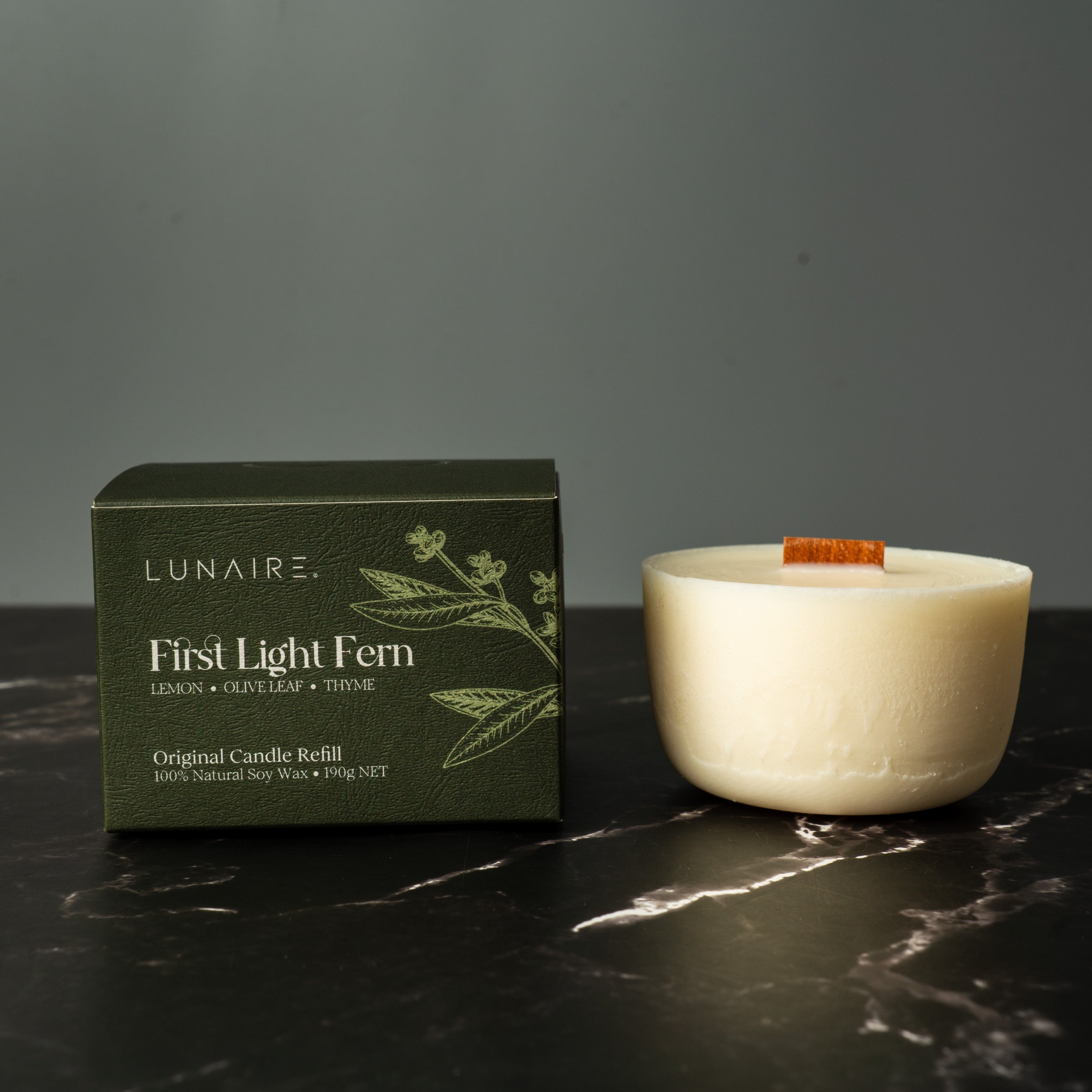 Lunaire refillabl candle and packaging on a dark marble surface with a gray background
