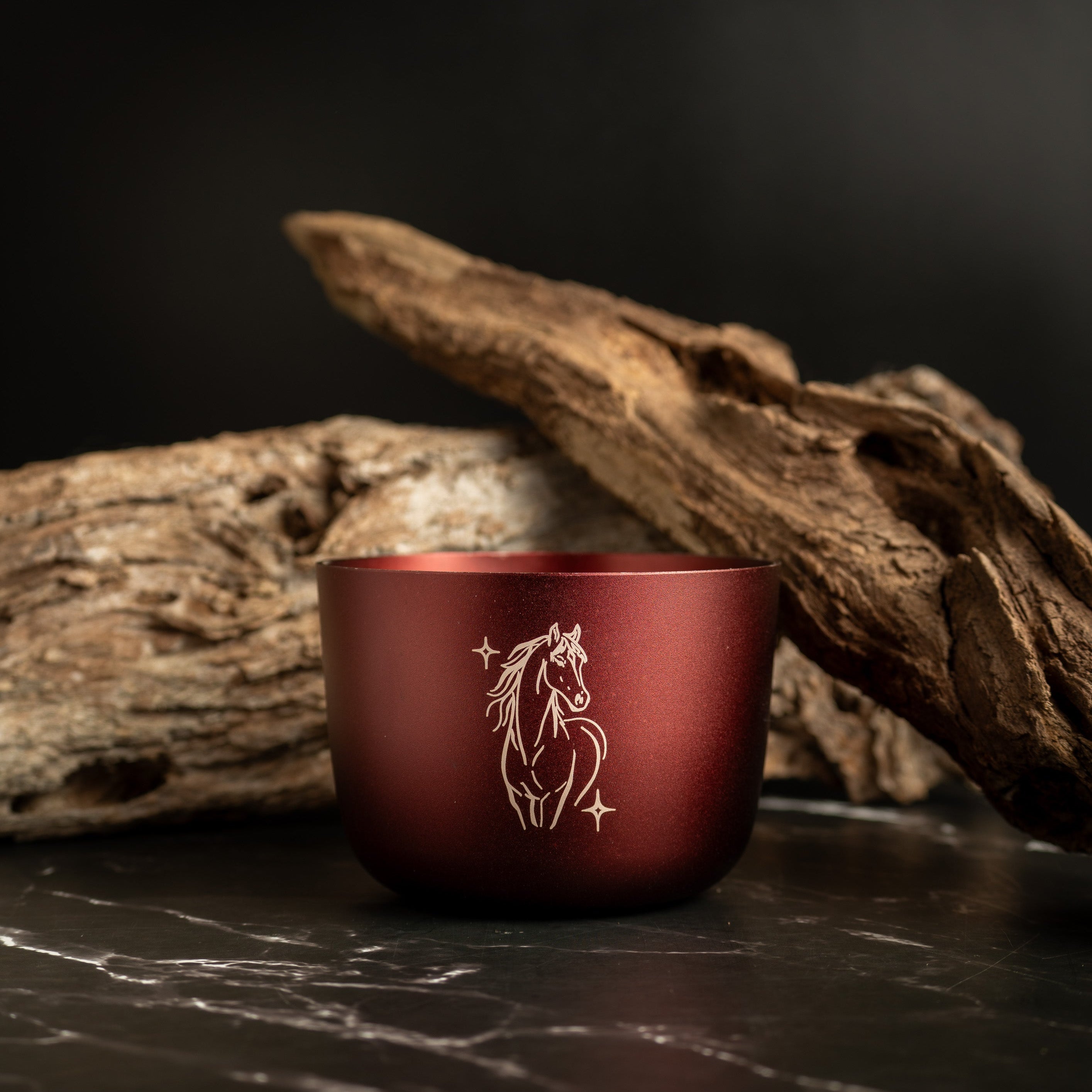 Burgundy Luxury  Cabdle with a horse design on a dark surface with wood in the background