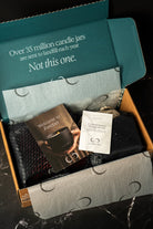 Unopened candle packaging with a card and small packet inside a box.