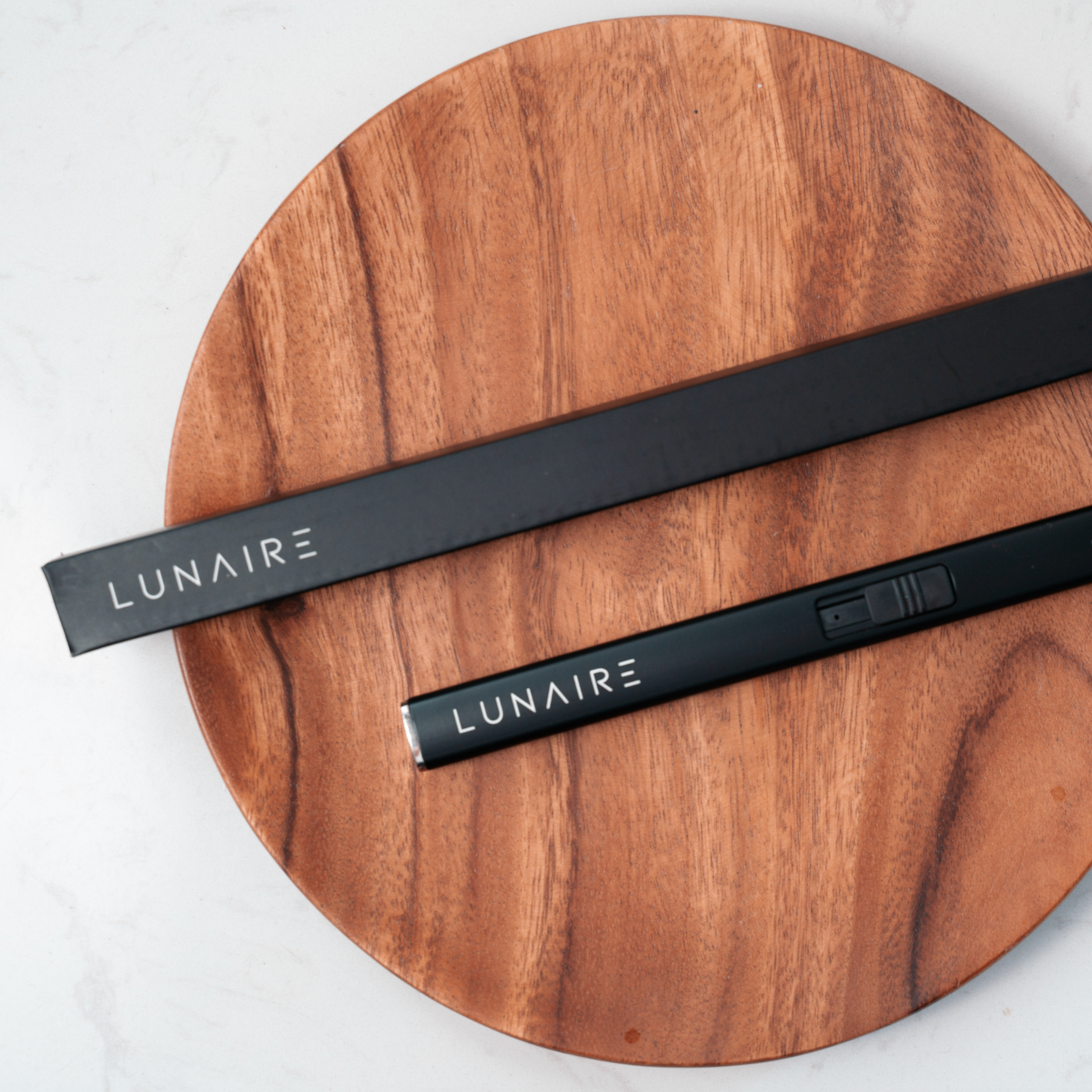 lunaire black rechargeable lighter and black rectangular box. laying on circular wooden plate