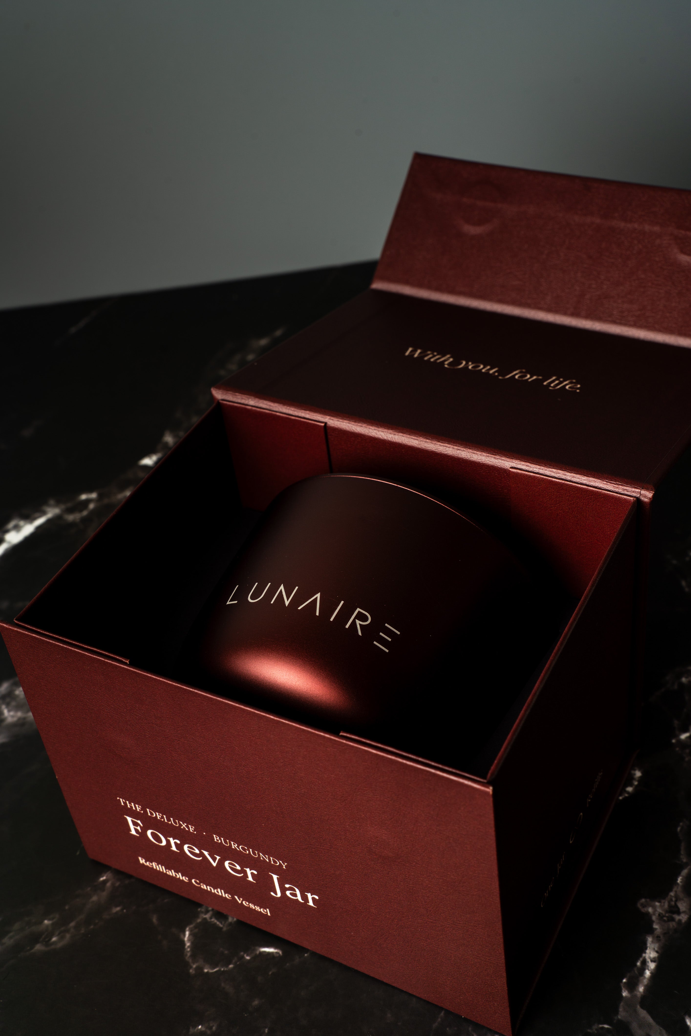 Lunaire aluminium refillable candle in a red box on a dark  marbled surface