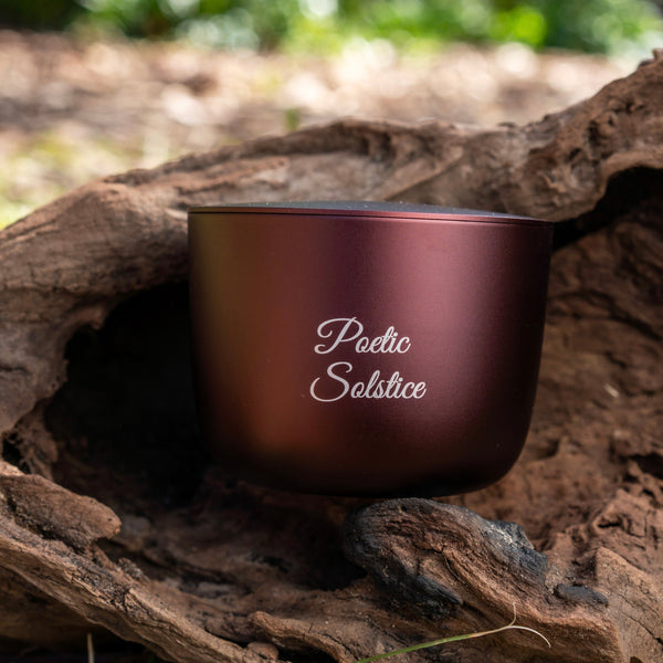burgundy aluminium candle with 'Poetic Solstice' text on a wooden log with a natural background