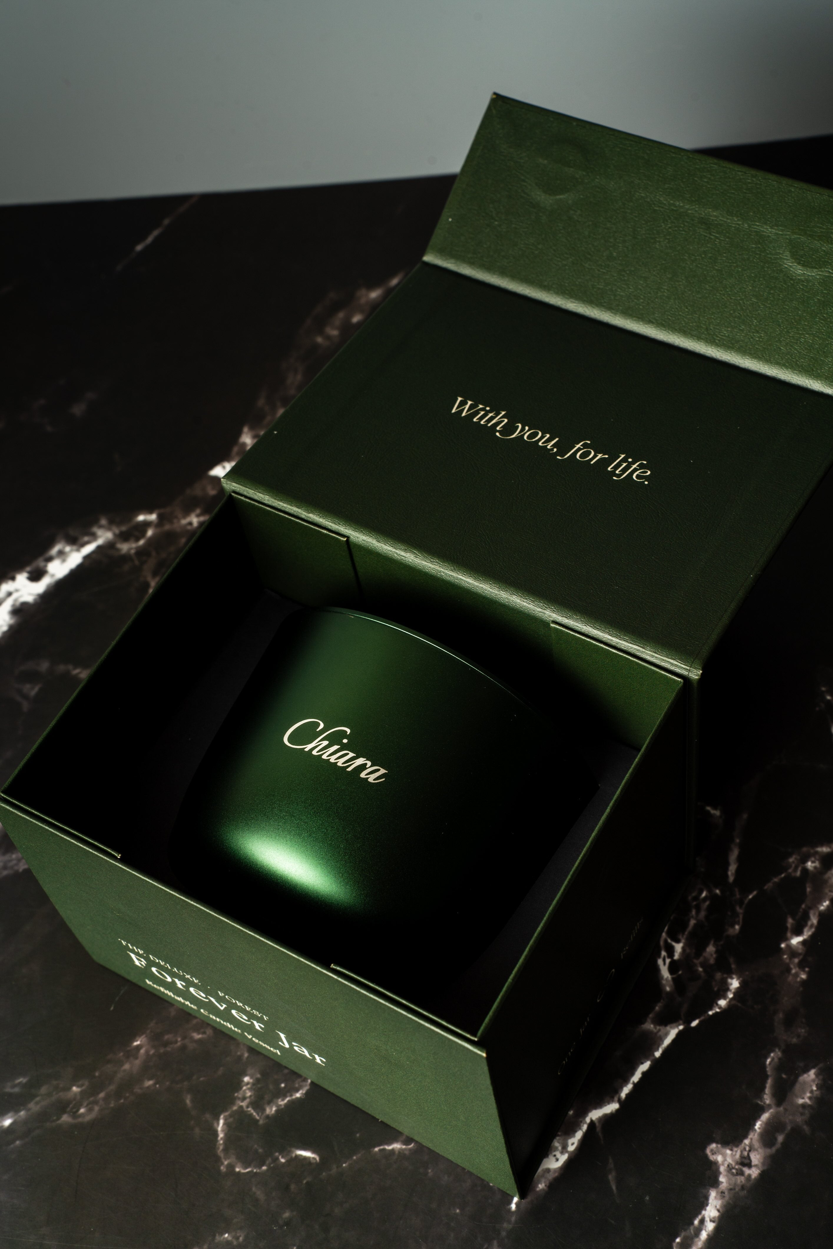 forest green forever candle with engraving 'Chiara' opened on a marbled bench top 