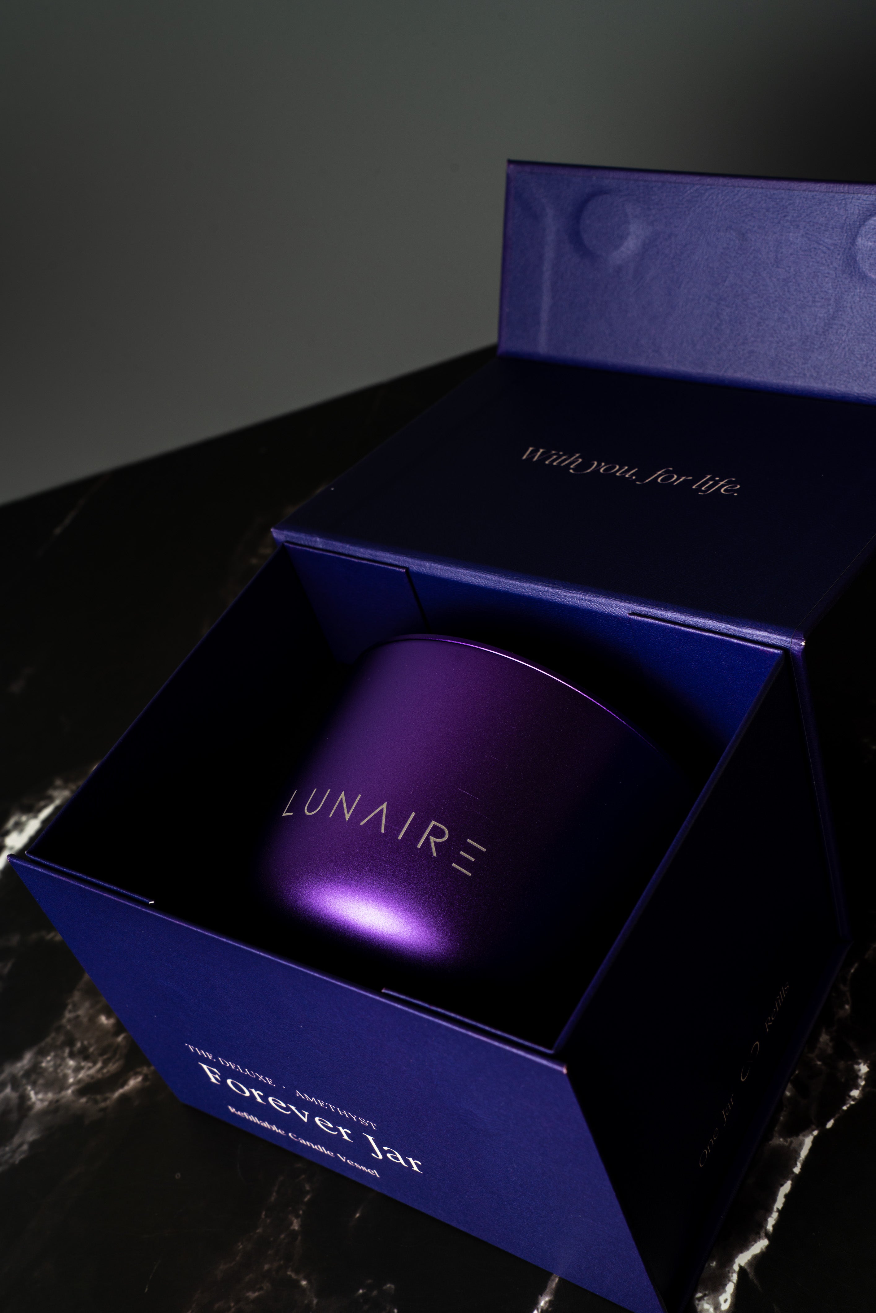 Lunaire Forever Candle  in a purple box with  branding on a dark background. refillable aluminium Candles. 